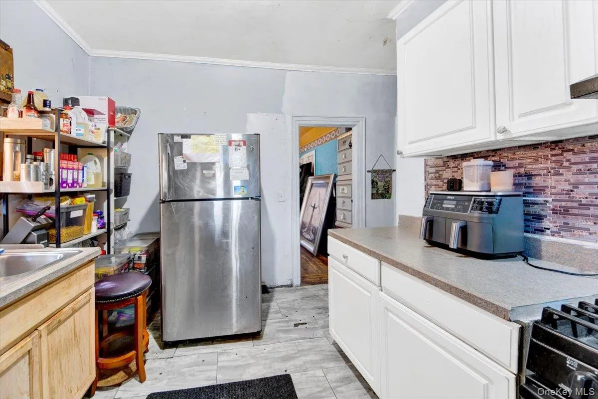 Kitchen with freestanding refrigerator, crown molding, light countertops, white cabinets, and backsplash Kitchen with freestanding refrigerator, crown molding, light countertops, white cabinets, and backsplash