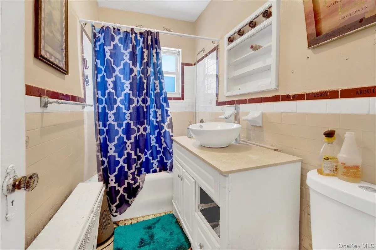 Bathroom featuring tile walls, vanity, wainscoting, and shower / bathtub combination with curtain Bathroom featuring tile walls, vanity, wainscoting, and shower / bathtub combination with curtain