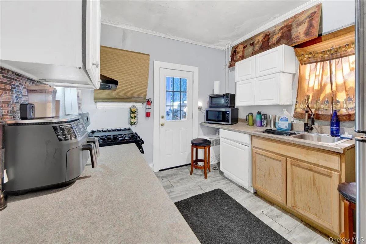 Kitchen with light countertops, black range with gas stovetop, stainless steel microwave, white cabinetry, and light brown cabinetry Kitchen with light countertops, black range with gas stovetop, stainless steel microwave, white cabinetry, and light brown cabinetry