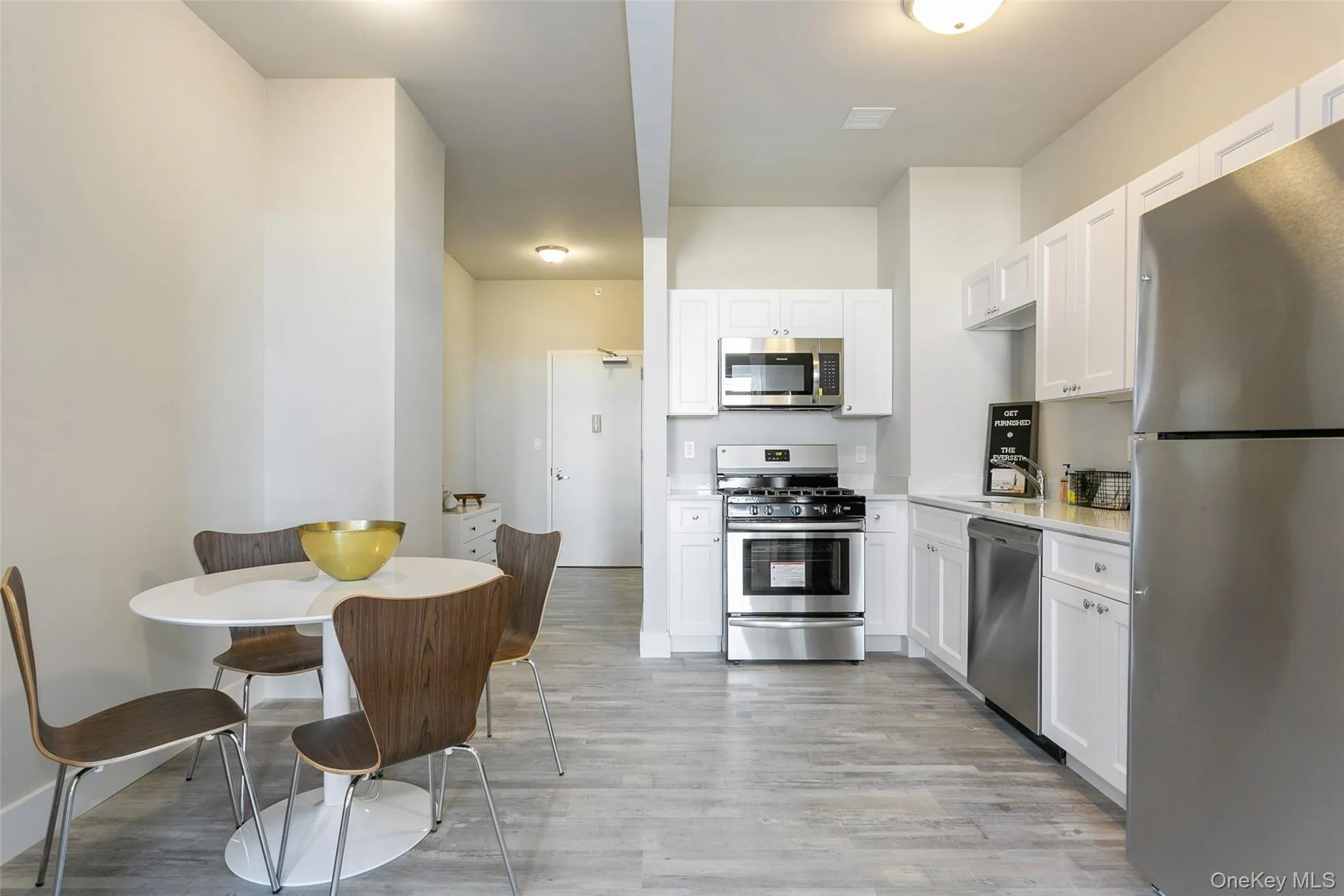 Kitchen featuring appliances with stainless steel finishes, white cabinetry, light wood finished floors, and light stone counters Kitchen featuring appliances with stainless steel finishes, white cabinetry, light wood finished floors, and light stone counters