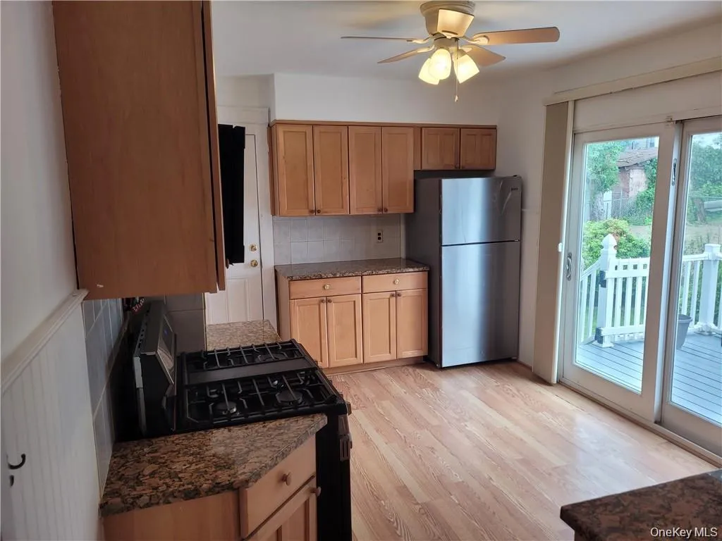 Kitchen with decorative backsplash, black range with gas cooktop, light wood finished floors, dark stone counters, and freestanding refrigerator Kitchen with decorative backsplash, black range with gas cooktop, light wood finished floors, dark stone counters, and freestanding refrigerator