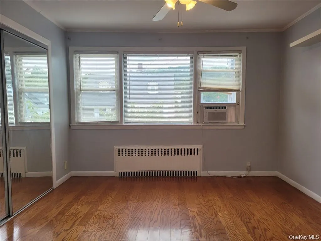Spare room with radiator, light wood finished floors, ornamental molding, ceiling fan, and cooling unit Spare room with radiator, light wood finished floors, ornamental molding, ceiling fan, and cooling unit