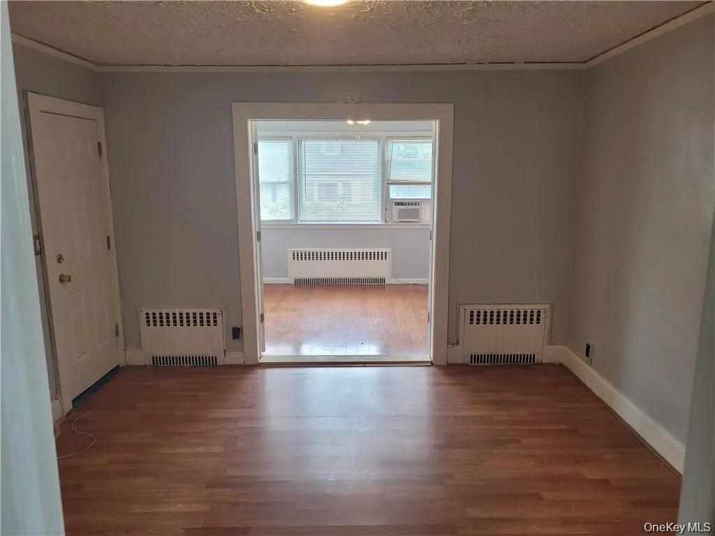 Unfurnished room featuring wood finished floors, crown molding, radiator, and a textured ceiling Unfurnished room featuring wood finished floors, crown molding, radiator, and a textured ceiling