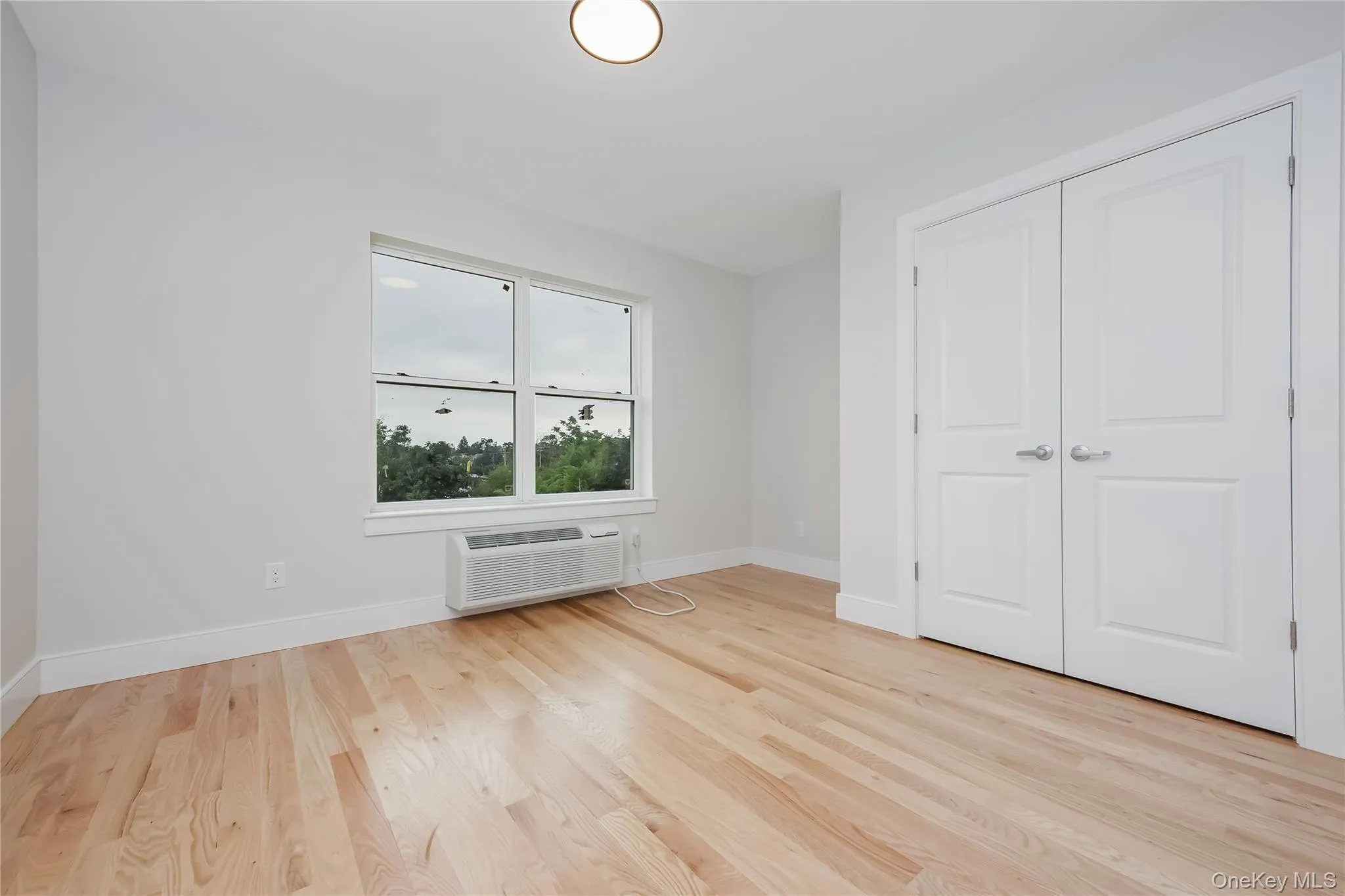 Unfurnished bedroom with light wood-style floors and a wall mounted air conditioner Unfurnished bedroom with light wood-style floors and a wall mounted air conditioner