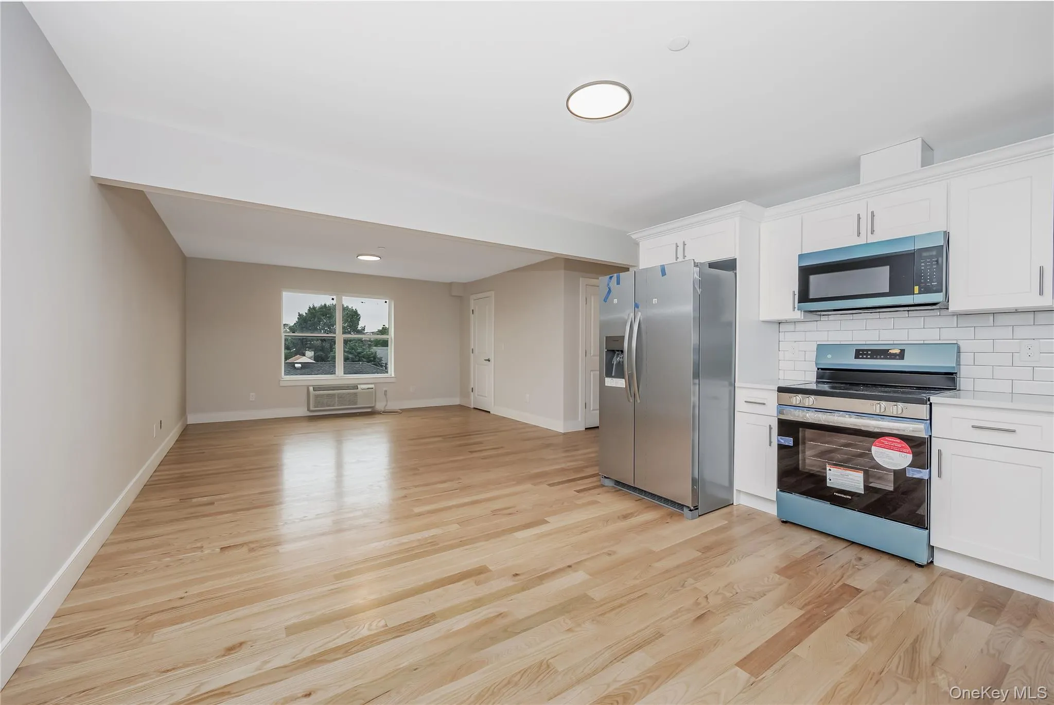 Kitchen featuring appliances with stainless steel finishes, white cabinetry, decorative backsplash, and light wood finished floors Kitchen featuring appliances with stainless steel finishes, white cabinetry, decorative backsplash, and light wood finished floors