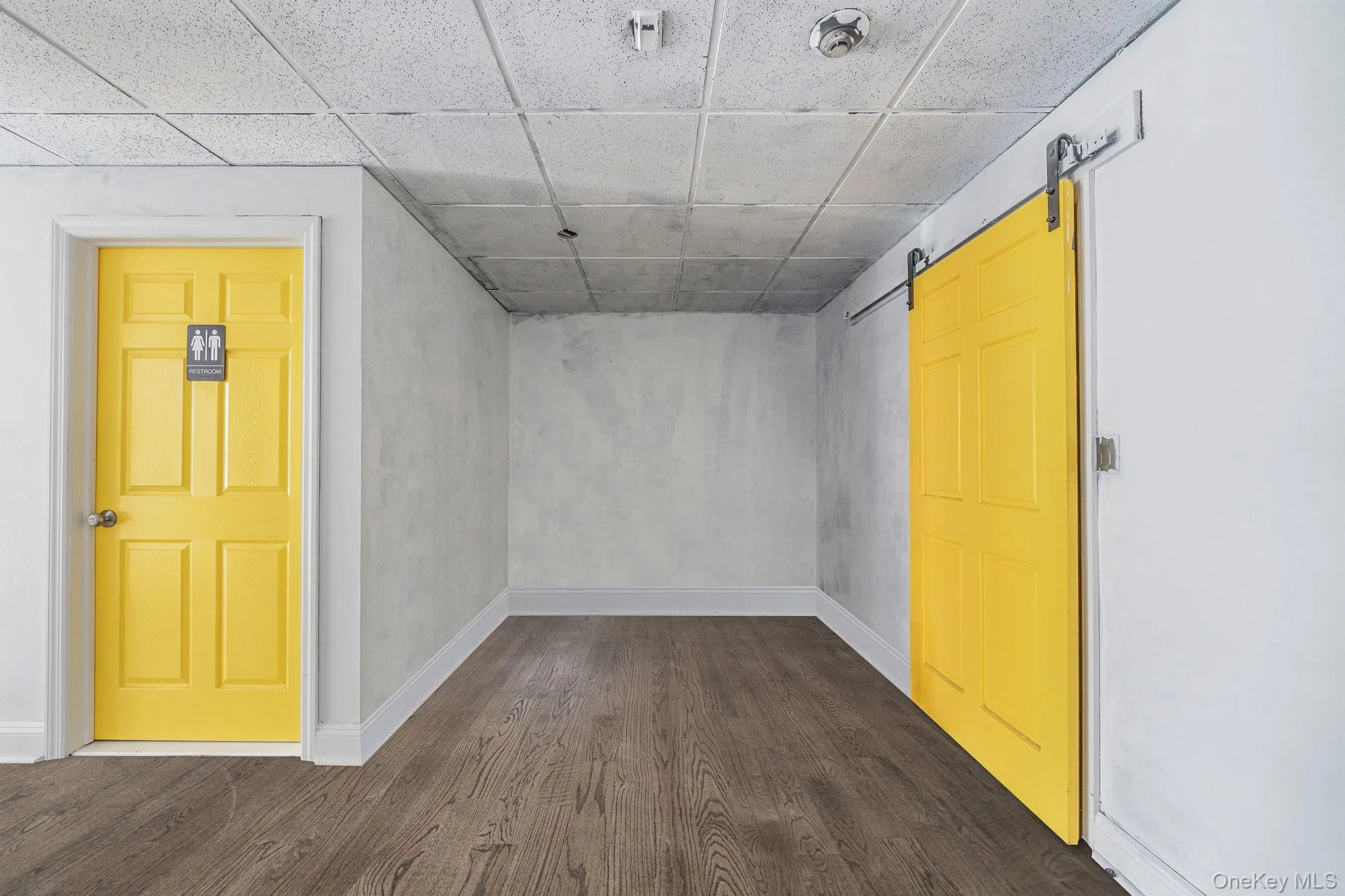 Unfurnished room with a barn door, a drop ceiling, and dark wood-type flooring Unfurnished room with a barn door, a drop ceiling, and dark wood-type flooring
