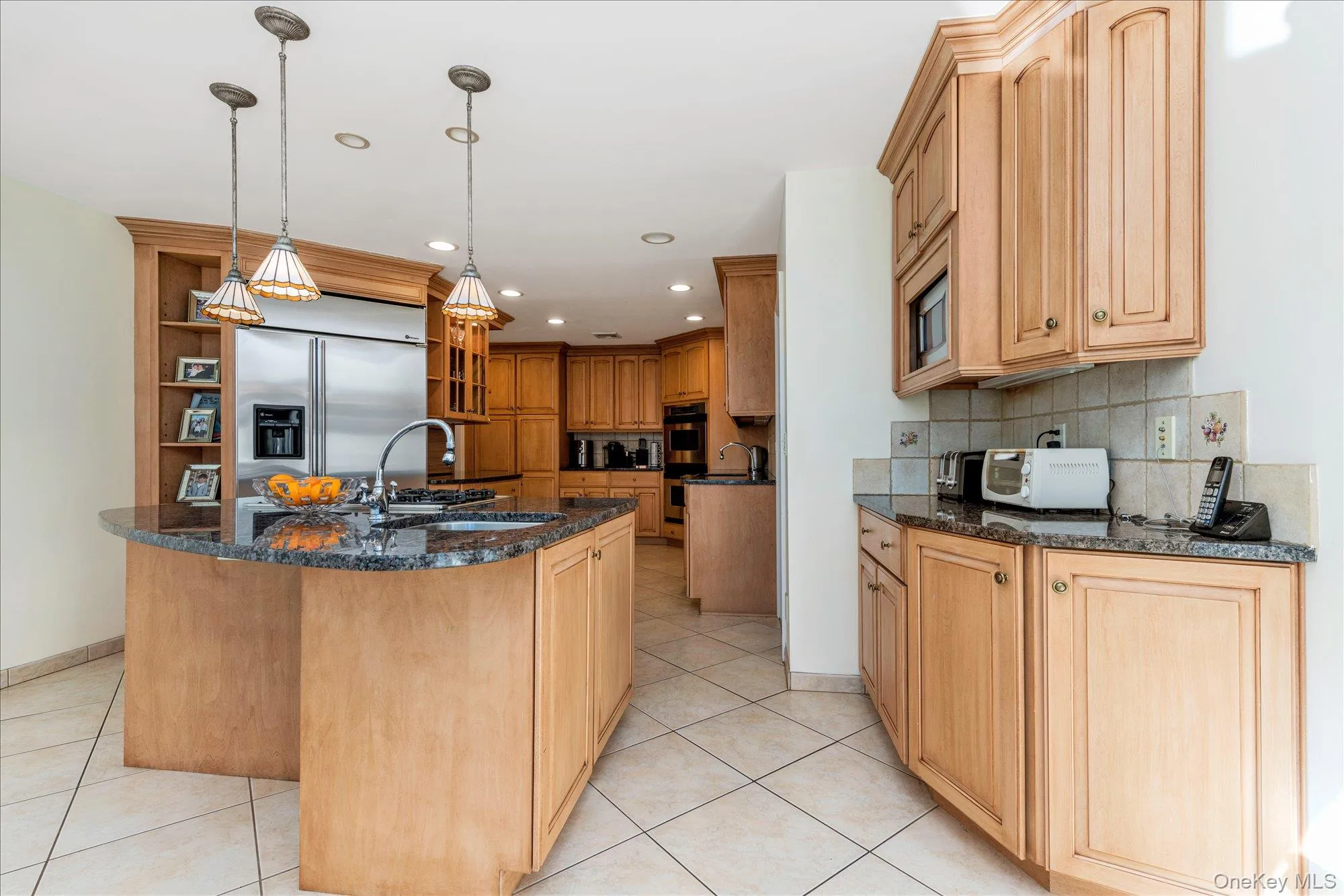 Kitchen with open shelves, a center island with sink, dark stone counters, decorative light fixtures, and built in appliances Kitchen with open shelves, a center island with sink, dark stone counters, decorative light fixtures, and built in appliances