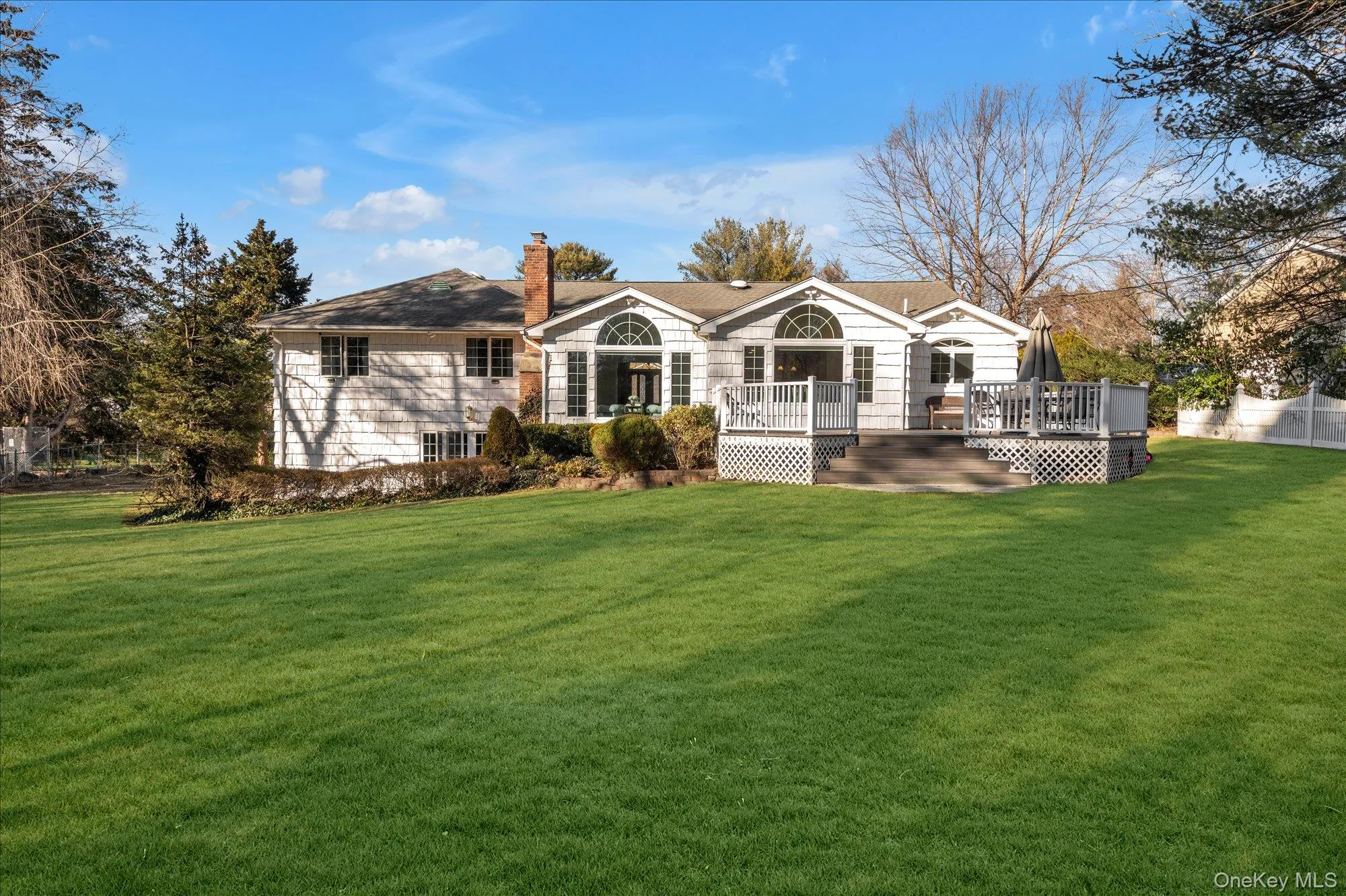 Rear view of property featuring a chimney, a wooden deck, and a lawn Rear view of property featuring a chimney, a wooden deck, and a lawn