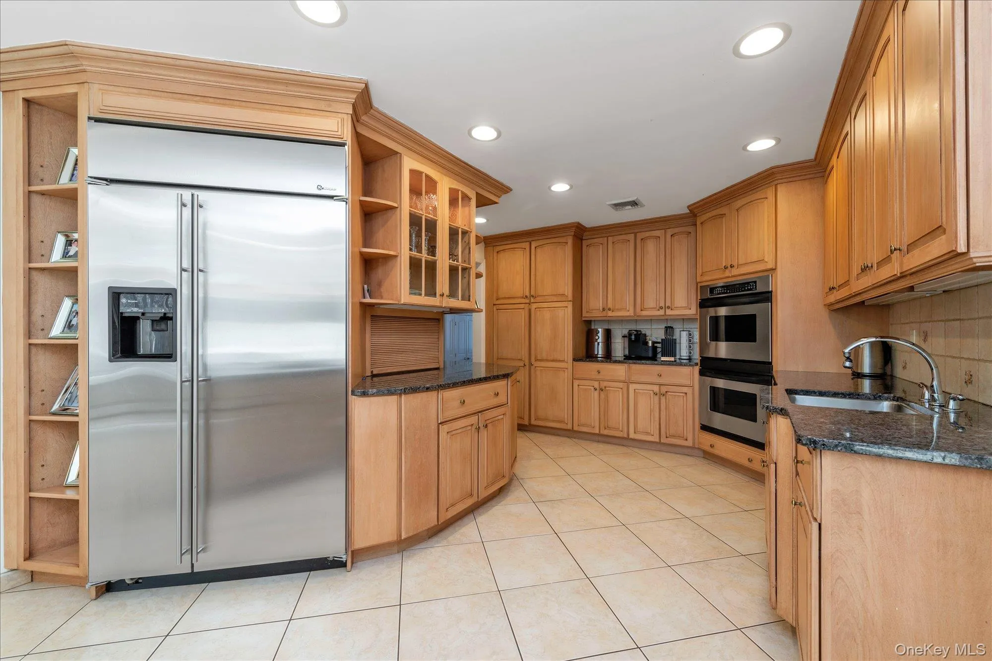 Kitchen with appliances with stainless steel finishes, dark stone counters, recessed lighting, light tile patterned floors, and glass insert cabinets Kitchen with appliances with stainless steel finishes, dark stone counters, recessed lighting, light tile patterned floors, and glass insert cabinets