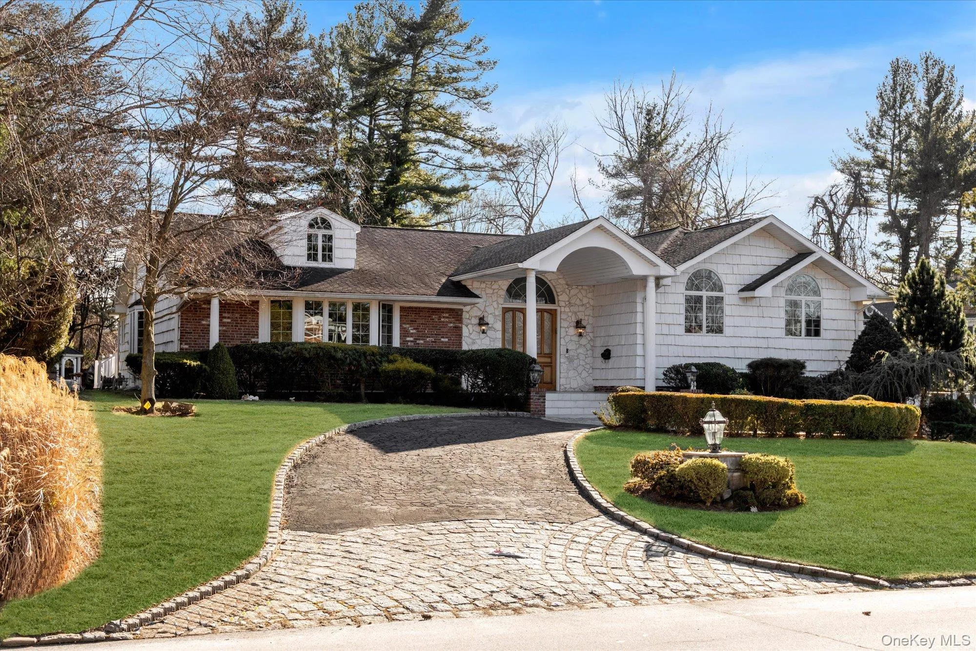 View of front of home with a front lawn, curved driveway, roof with shingles, and brick siding View of front of home with a front lawn, curved driveway, roof with shingles, and brick siding