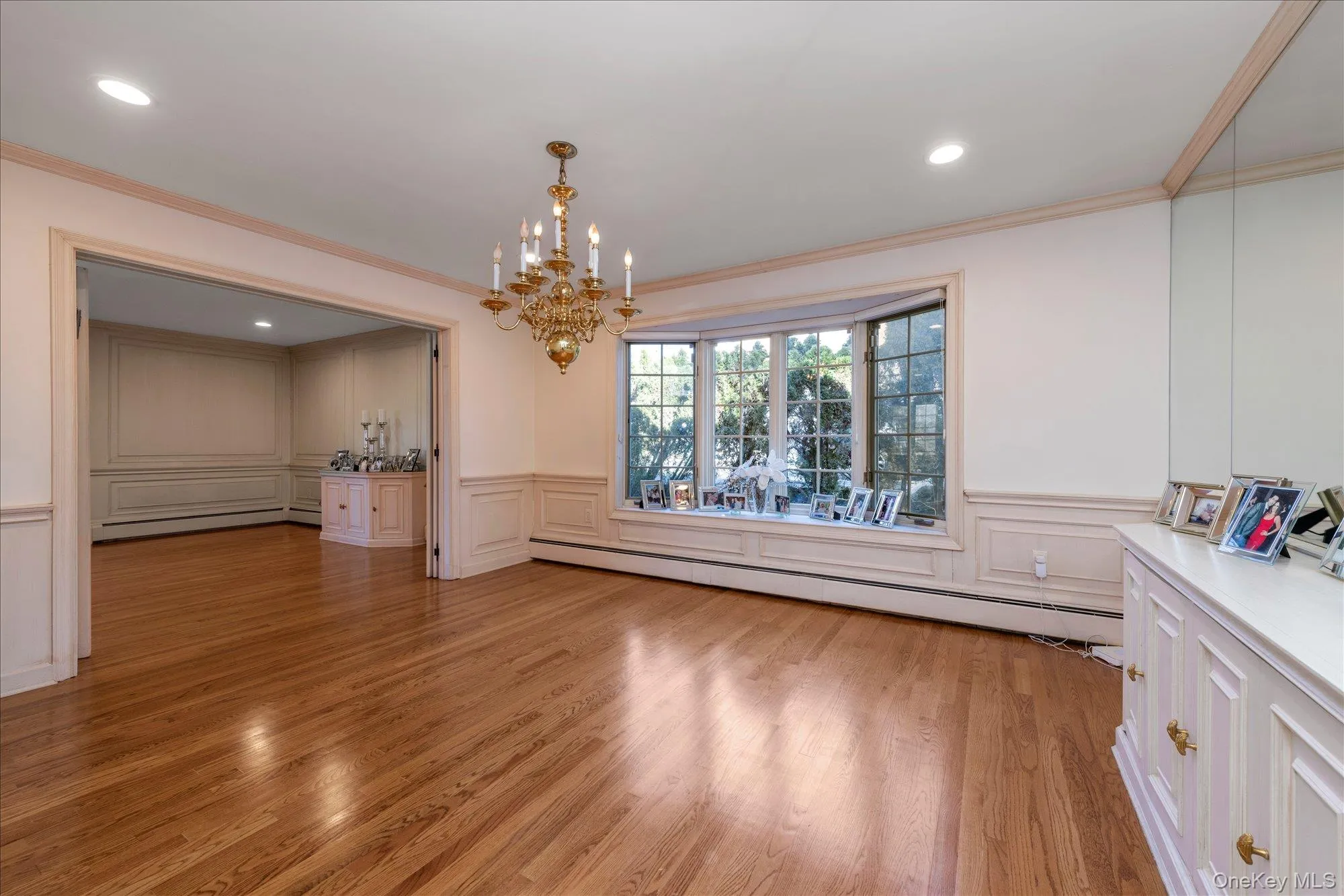 Unfurnished dining area with light wood-style floors, a chandelier, ornamental molding, baseboard heating, and a decorative wall Unfurnished dining area with light wood-style floors, a chandelier, ornamental molding, baseboard heating, and a decorative wall