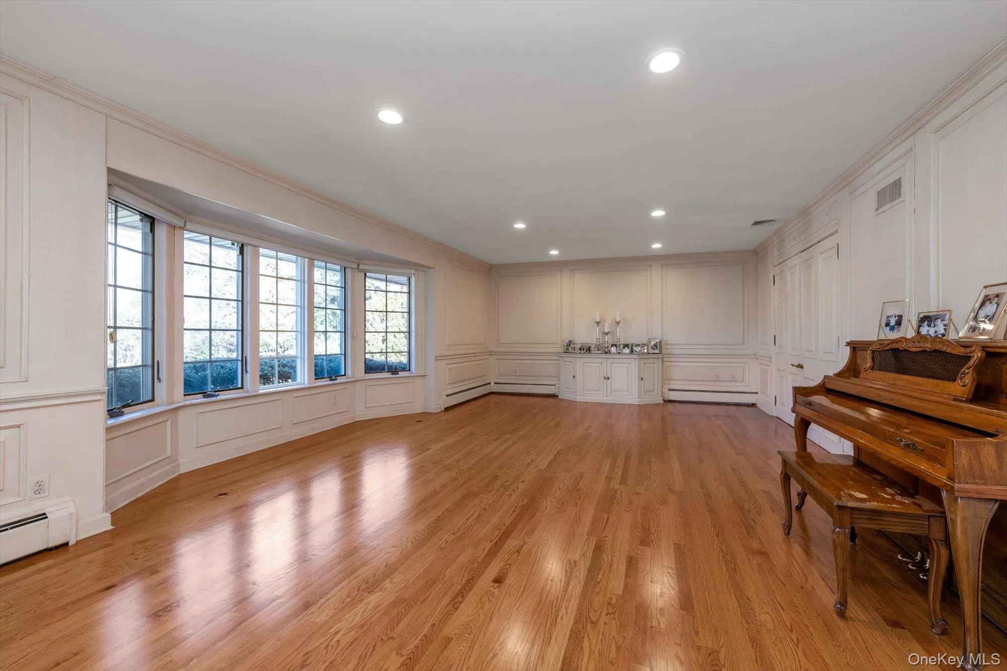 Living area with a decorative wall, ornamental molding, light wood-style floors, recessed lighting, and a baseboard radiator Living area with a decorative wall, ornamental molding, light wood-style floors, recessed lighting, and a baseboard radiator