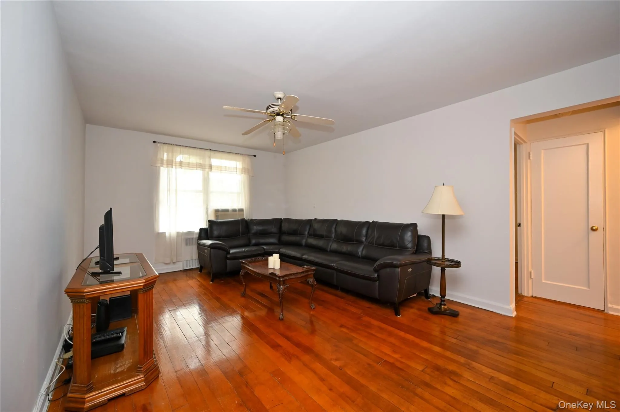 Living room with hardwood / wood-style flooring, a ceiling fan, and radiator heating unit Living room with hardwood / wood-style flooring, a ceiling fan, and radiator heating unit