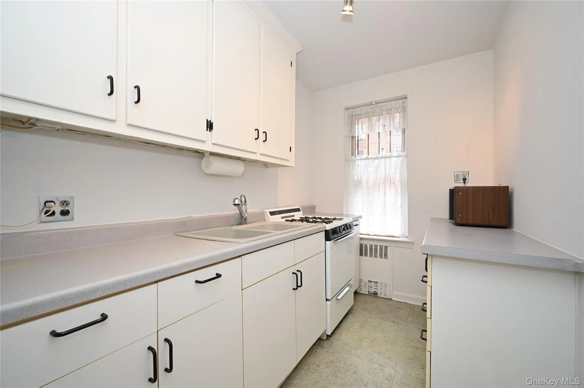 Kitchen featuring white cabinets, white range with gas stovetop, light countertops, and radiator Kitchen featuring white cabinets, white range with gas stovetop, light countertops, and radiator