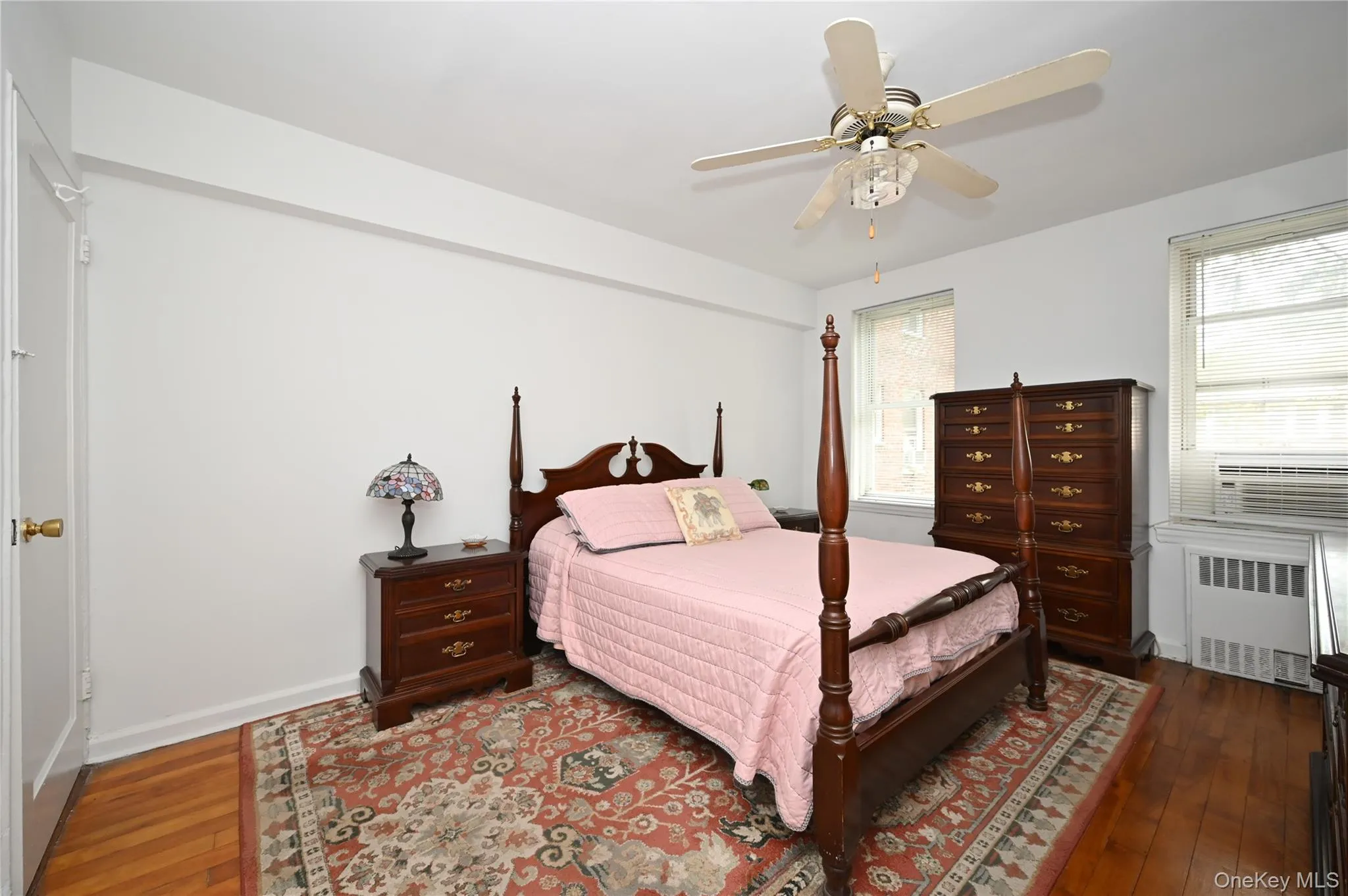 Bedroom with dark wood-style floors, radiator heating unit, ceiling fan, and cooling unit Bedroom with dark wood-style floors, radiator heating unit, ceiling fan, and cooling unit