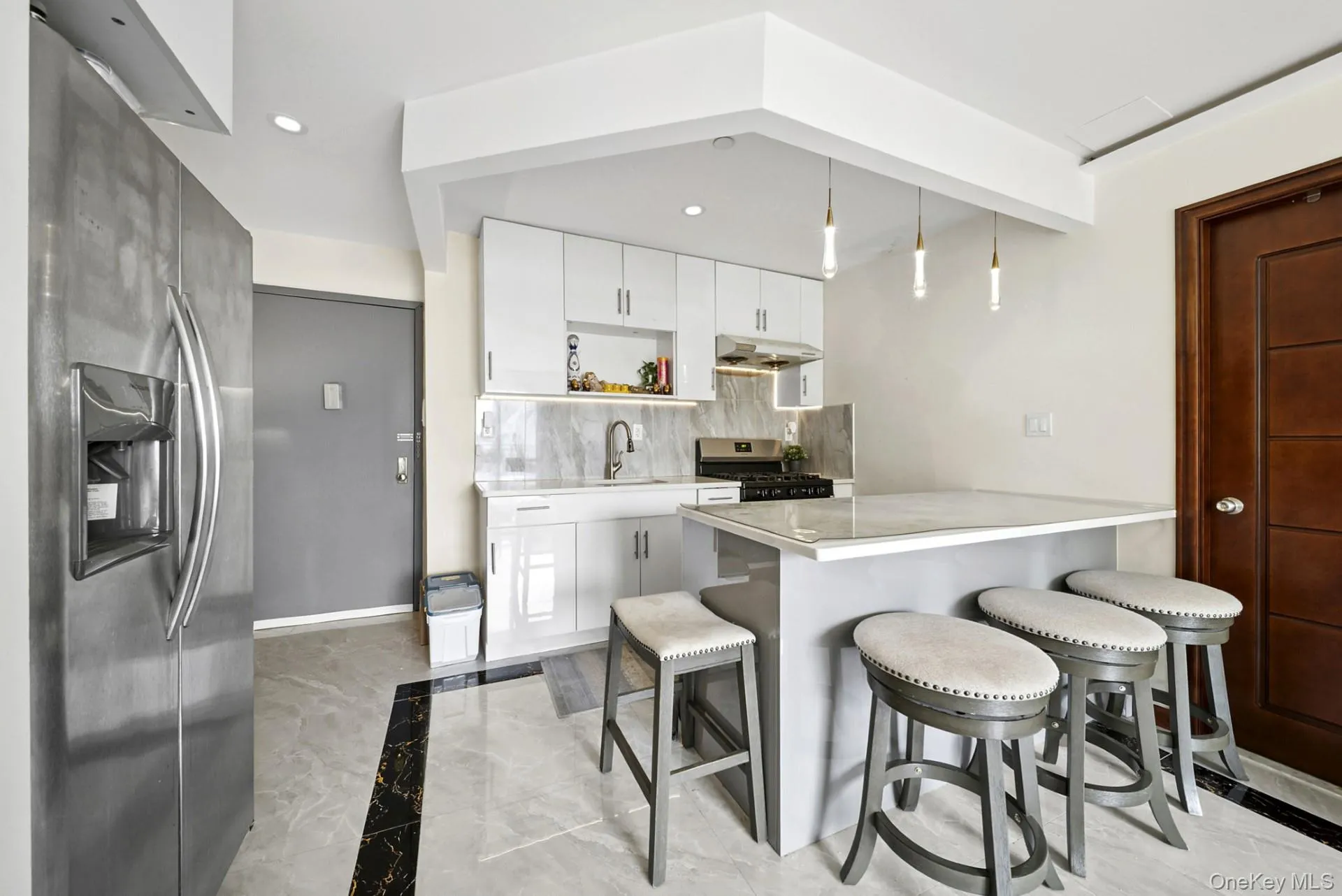 Kitchen featuring light marble finish flooring, a peninsula, stainless steel appliances, a breakfast bar area, and recessed lighting Kitchen featuring light marble finish flooring, a peninsula, stainless steel appliances, a breakfast bar area, and recessed lighting