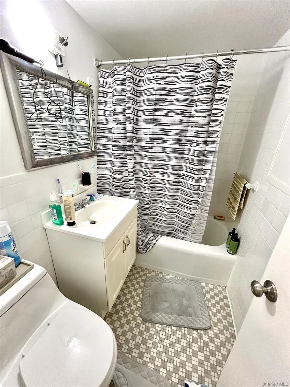 Bathroom featuring tile walls, shower / bath combo with shower curtain, vanity, and tile patterned floors Bathroom featuring tile walls, shower / bath combo with shower curtain, vanity, and tile patterned floors