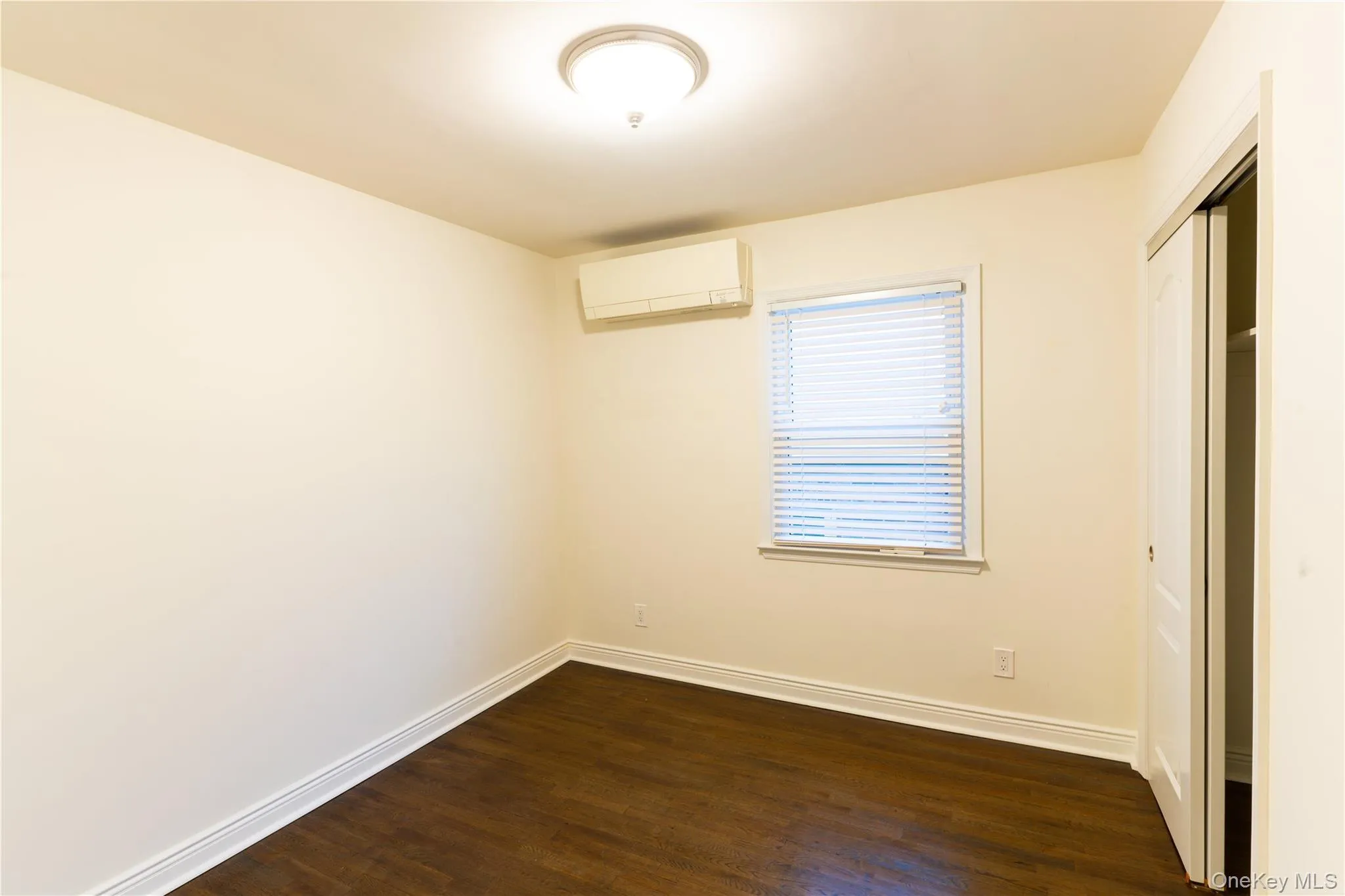 Unfurnished bedroom featuring dark wood-type flooring, a closet, and a wall unit AC Unfurnished bedroom featuring dark wood-type flooring, a closet, and a wall unit AC