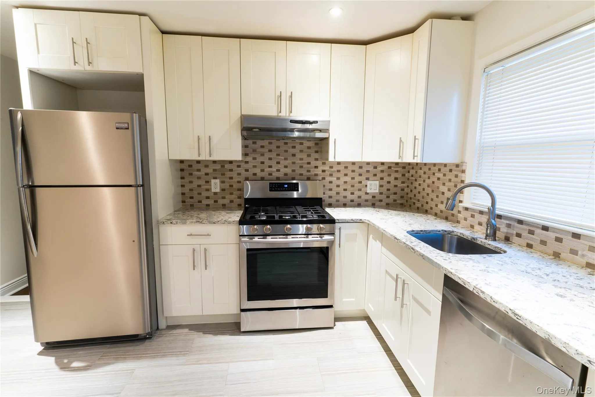 Kitchen with appliances with stainless steel finishes, backsplash, light stone counters, white cabinetry, and recessed lighting Kitchen with appliances with stainless steel finishes, backsplash, light stone counters, white cabinetry, and recessed lighting