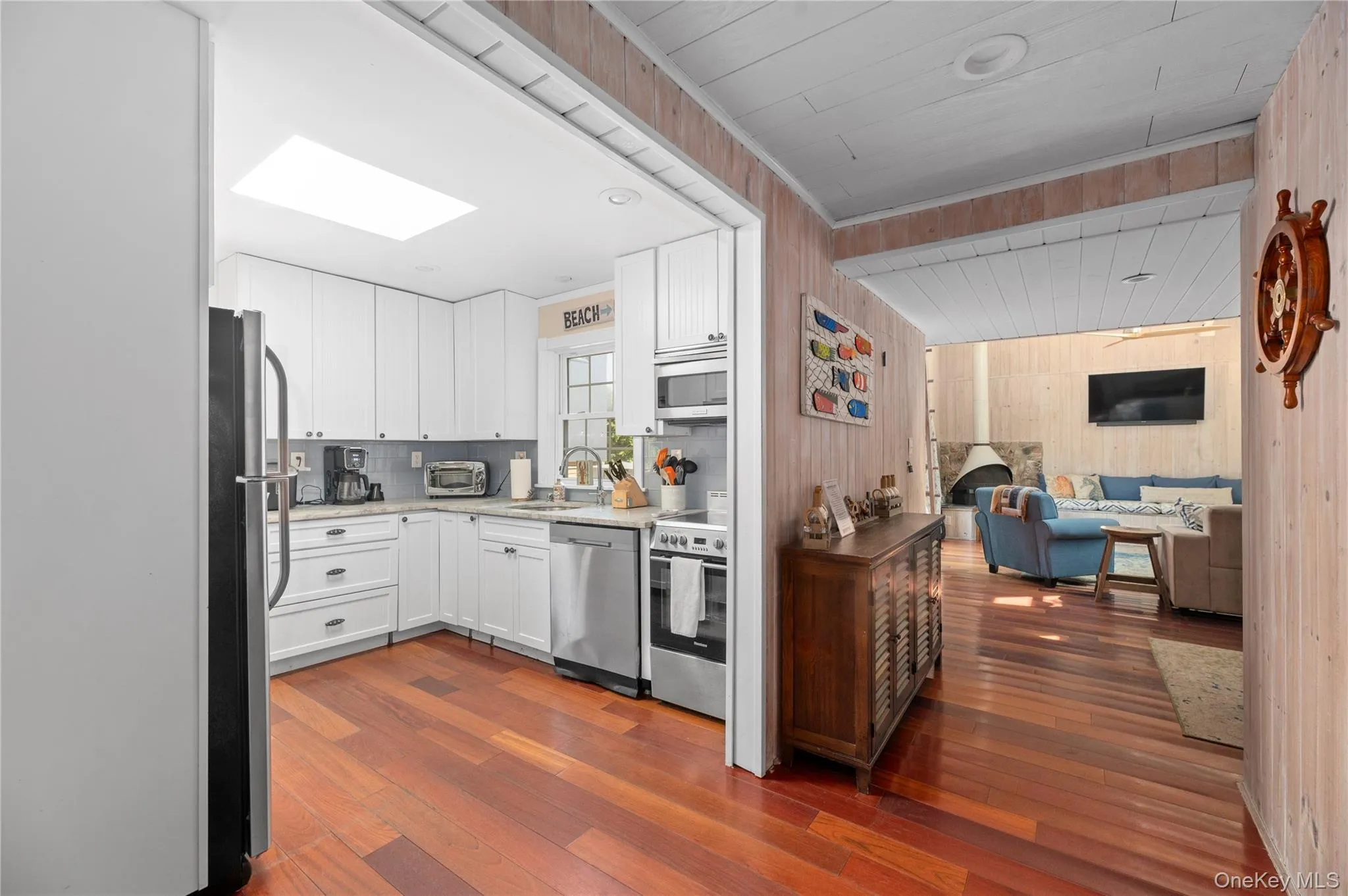 Kitchen featuring white cabinets, dark wood-style flooring, appliances with stainless steel finishes, light stone counters, and wood walls Kitchen featuring white cabinets, dark wood-style flooring, appliances with stainless steel finishes, light stone counters, and wood walls