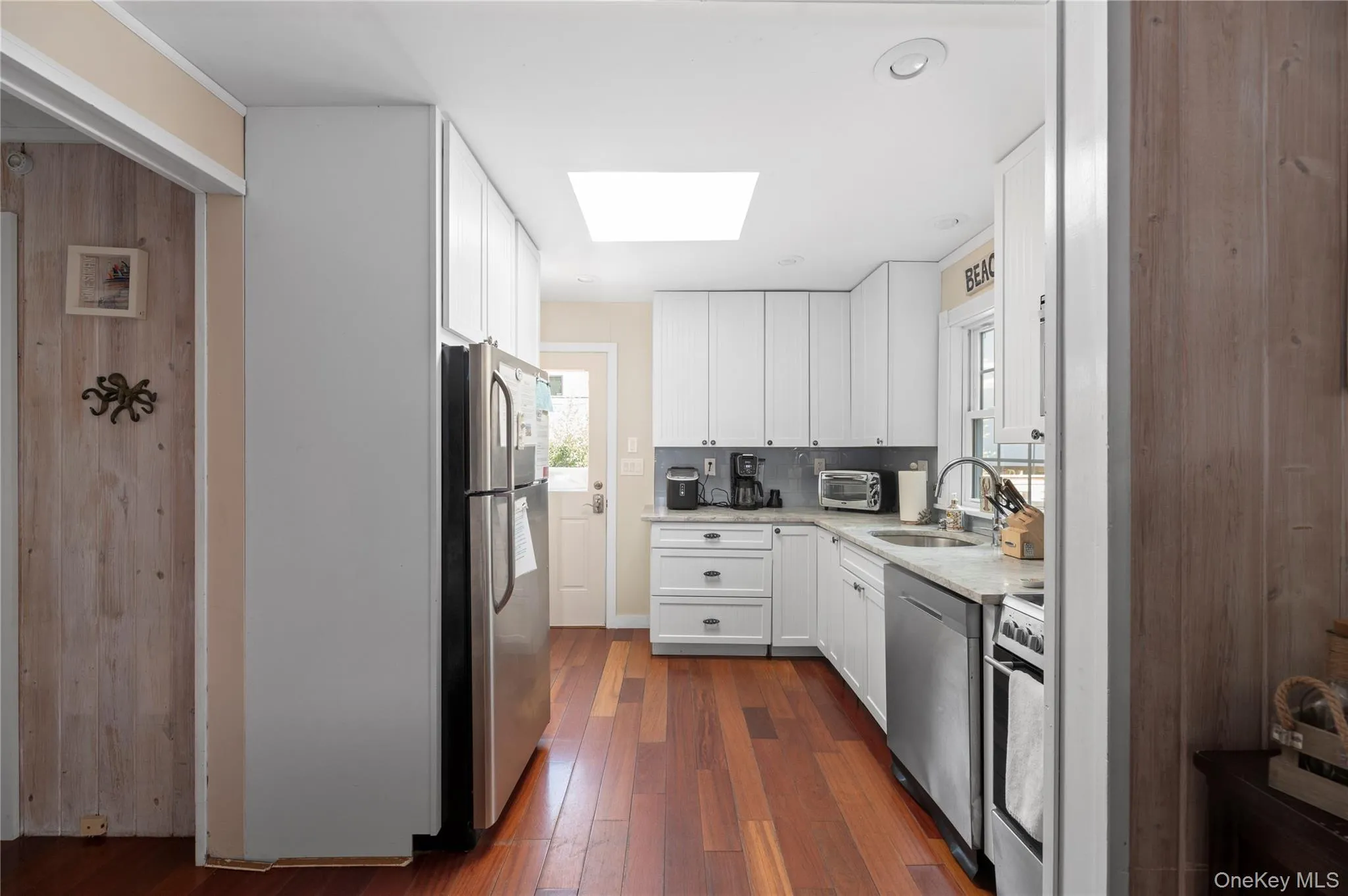 Kitchen featuring a skylight, dark wood-type flooring, white cabinetry, appliances with stainless steel finishes, and light stone countertops Kitchen featuring a skylight, dark wood-type flooring, white cabinetry, appliances with stainless steel finishes, and light stone countertops
