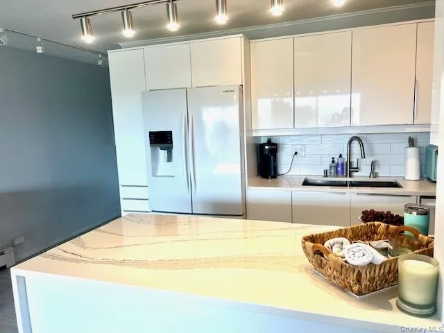 Kitchen featuring track lighting, refrigerator with ice dispenser, modern cabinets, light stone counters, and white cabinets Kitchen featuring track lighting, refrigerator with ice dispenser, modern cabinets, light stone counters, and white cabinets