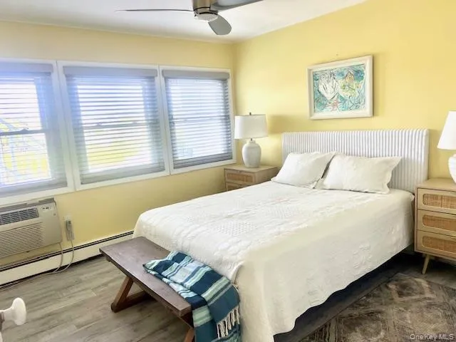 Bedroom with wood finished floors, a baseboard heating unit, a ceiling fan, and an AC wall unit Bedroom with wood finished floors, a baseboard heating unit, a ceiling fan, and an AC wall unit