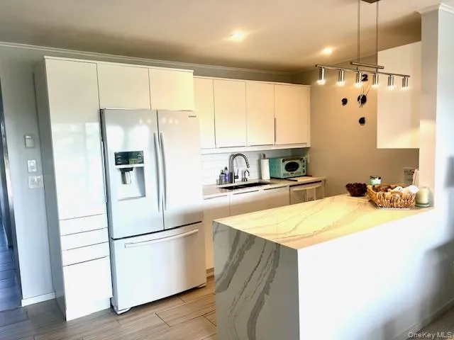 Kitchen with refrigerator with ice dispenser, white cabinets, a peninsula, wood finish floors, and modern cabinets Kitchen with refrigerator with ice dispenser, white cabinets, a peninsula, wood finish floors, and modern cabinets