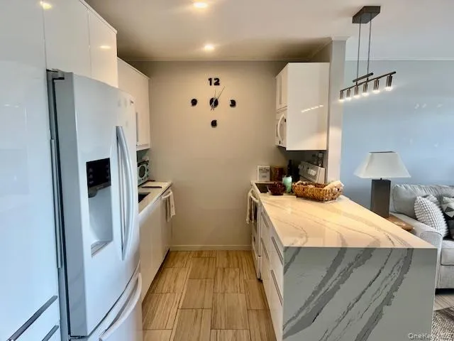 Kitchen with white cabinets, light stone countertops, white appliances, decorative light fixtures, and a peninsula Kitchen with white cabinets, light stone countertops, white appliances, decorative light fixtures, and a peninsula