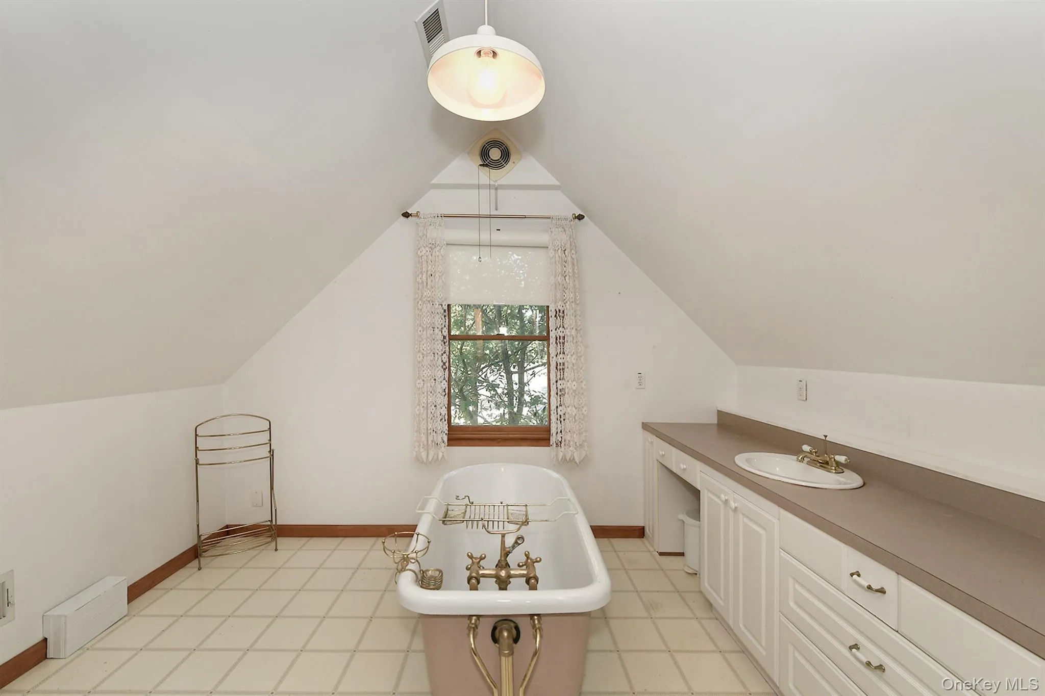 Bathroom featuring a freestanding tub, vaulted ceiling, light tile patterned floors, vanity, and a baseboard heating unit Bathroom featuring a freestanding tub, vaulted ceiling, light tile patterned floors, vanity, and a baseboard heating unit