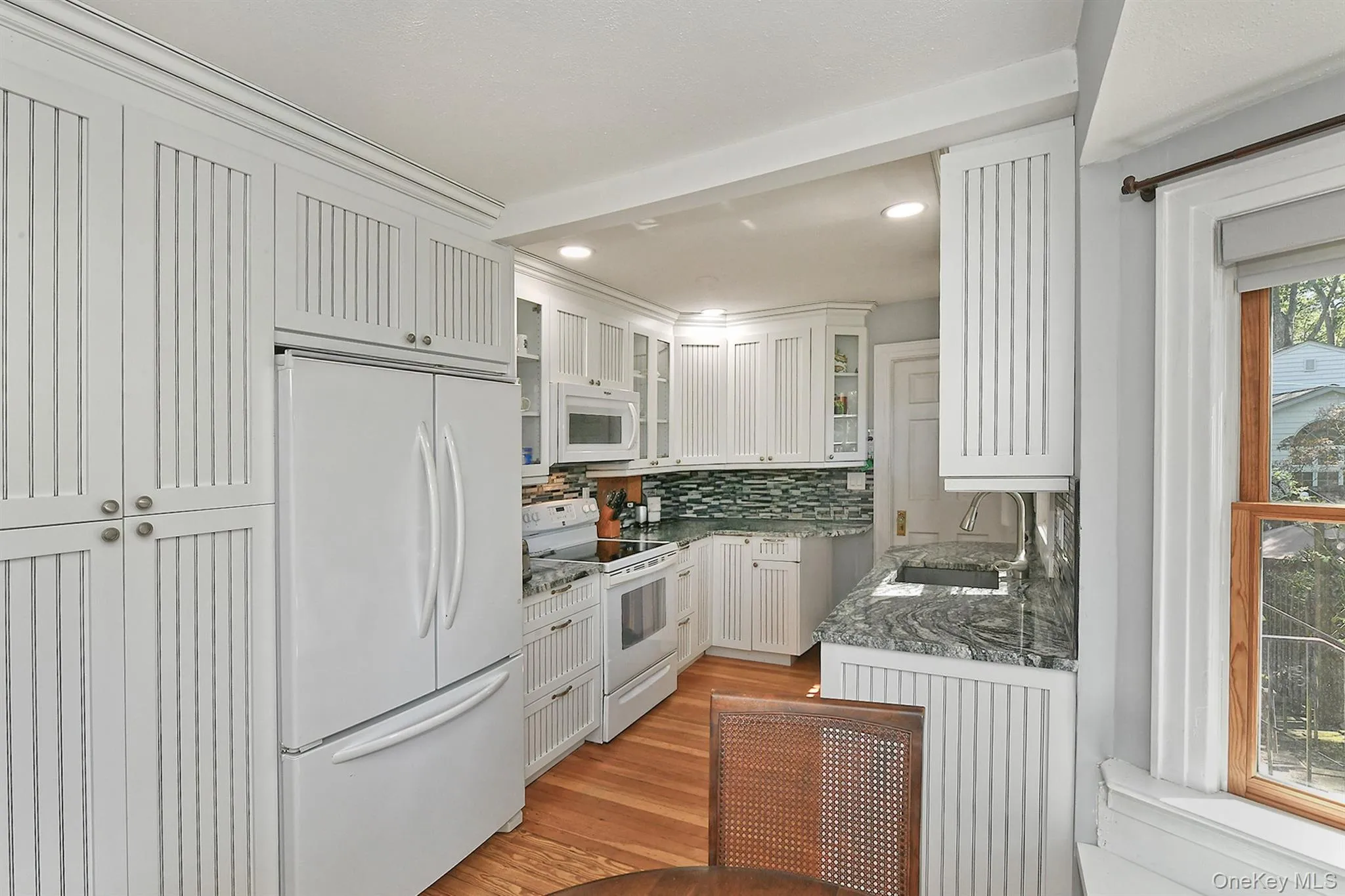 Kitchen with white appliances, light stone counters, backsplash, light wood-type flooring, and recessed lighting Kitchen with white appliances, light stone counters, backsplash, light wood-type flooring, and recessed lighting