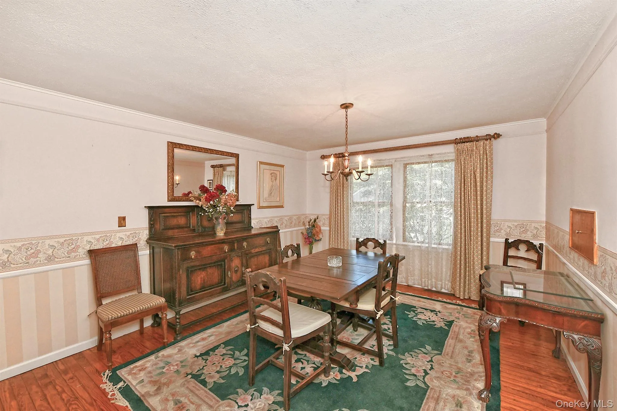 Dining space featuring a wainscoted wall, hardwood / wood-style floors, wallpapered walls, a chandelier, and a textured ceiling Dining space featuring a wainscoted wall, hardwood / wood-style floors, wallpapered walls, a chandelier, and a textured ceiling