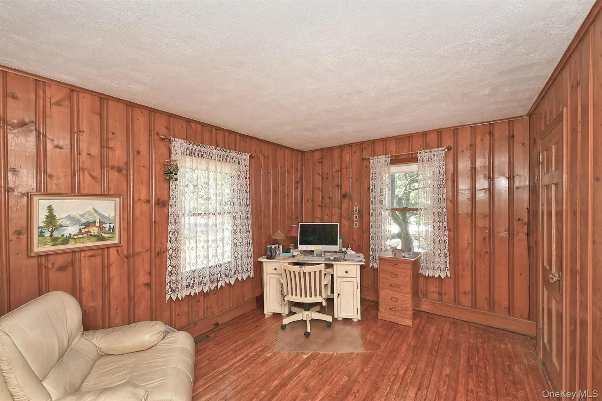 Office area featuring wood-type flooring, wooden walls, and a textured ceiling Office area featuring wood-type flooring, wooden walls, and a textured ceiling