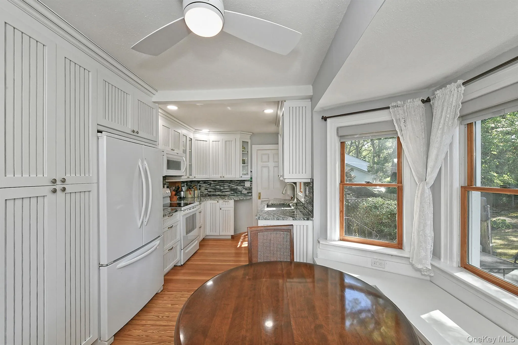 Kitchen with white appliances, decorative backsplash, light wood finished floors, light stone countertops, and white cabinetry Kitchen with white appliances, decorative backsplash, light wood finished floors, light stone countertops, and white cabinetry