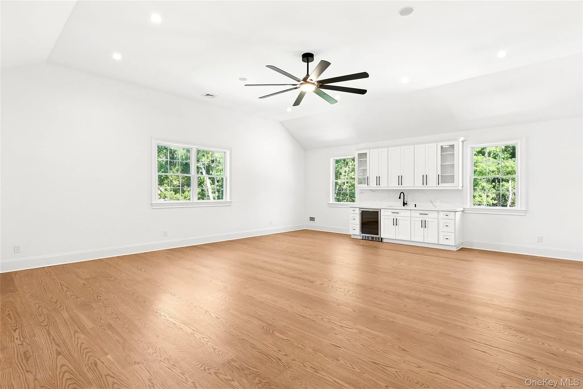Unfurnished living room with vaulted ceiling, plenty of natural light, light wood-type flooring, recessed lighting, and wine cooler Unfurnished living room with vaulted ceiling, plenty of natural light, light wood-type flooring, recessed lighting, and wine cooler