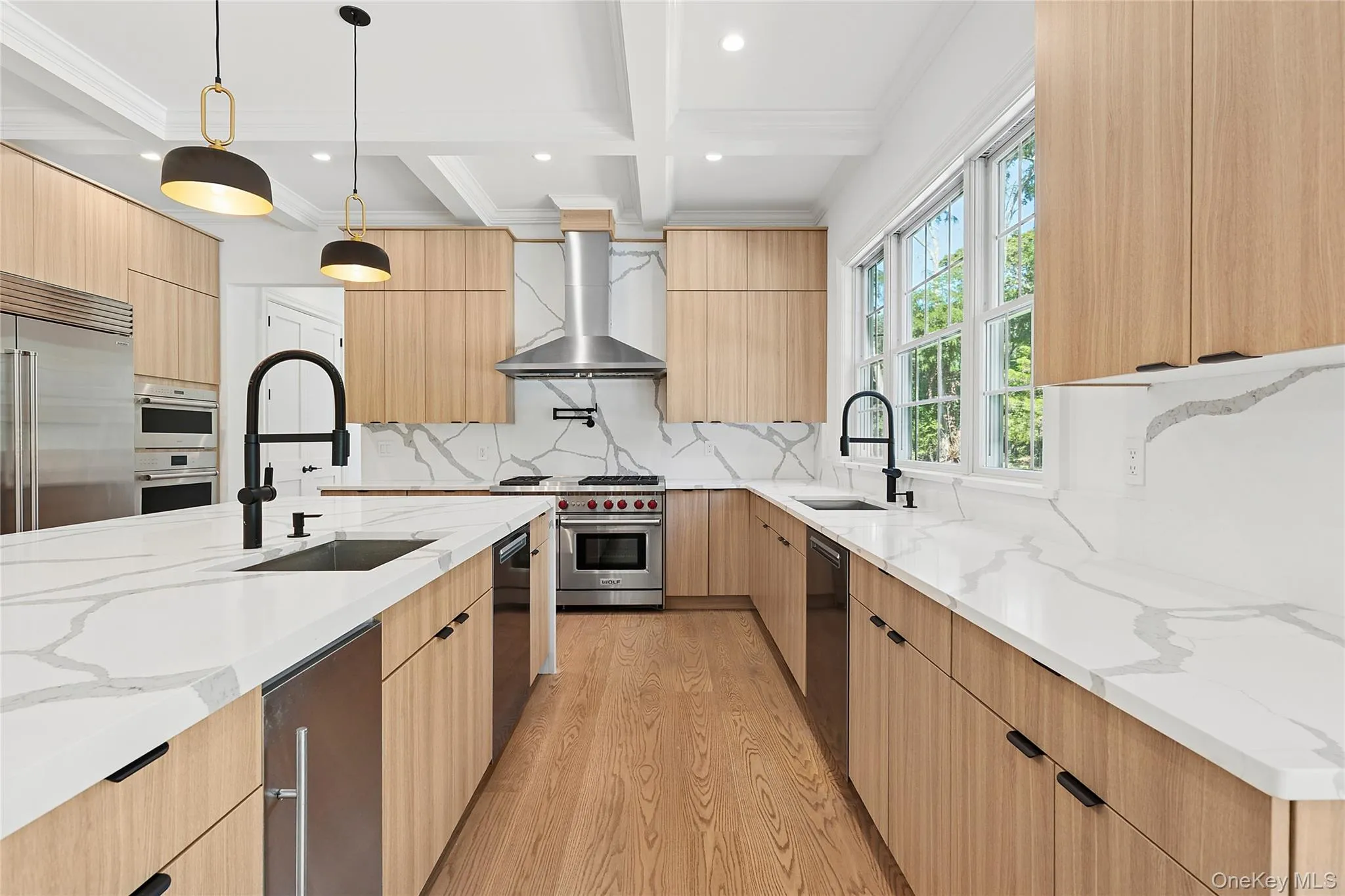 Kitchen with light stone counters, modern cabinets, light wood-style floors, decorative light fixtures, and light brown cabinetry Kitchen with light stone counters, modern cabinets, light wood-style floors, decorative light fixtures, and light brown cabinetry