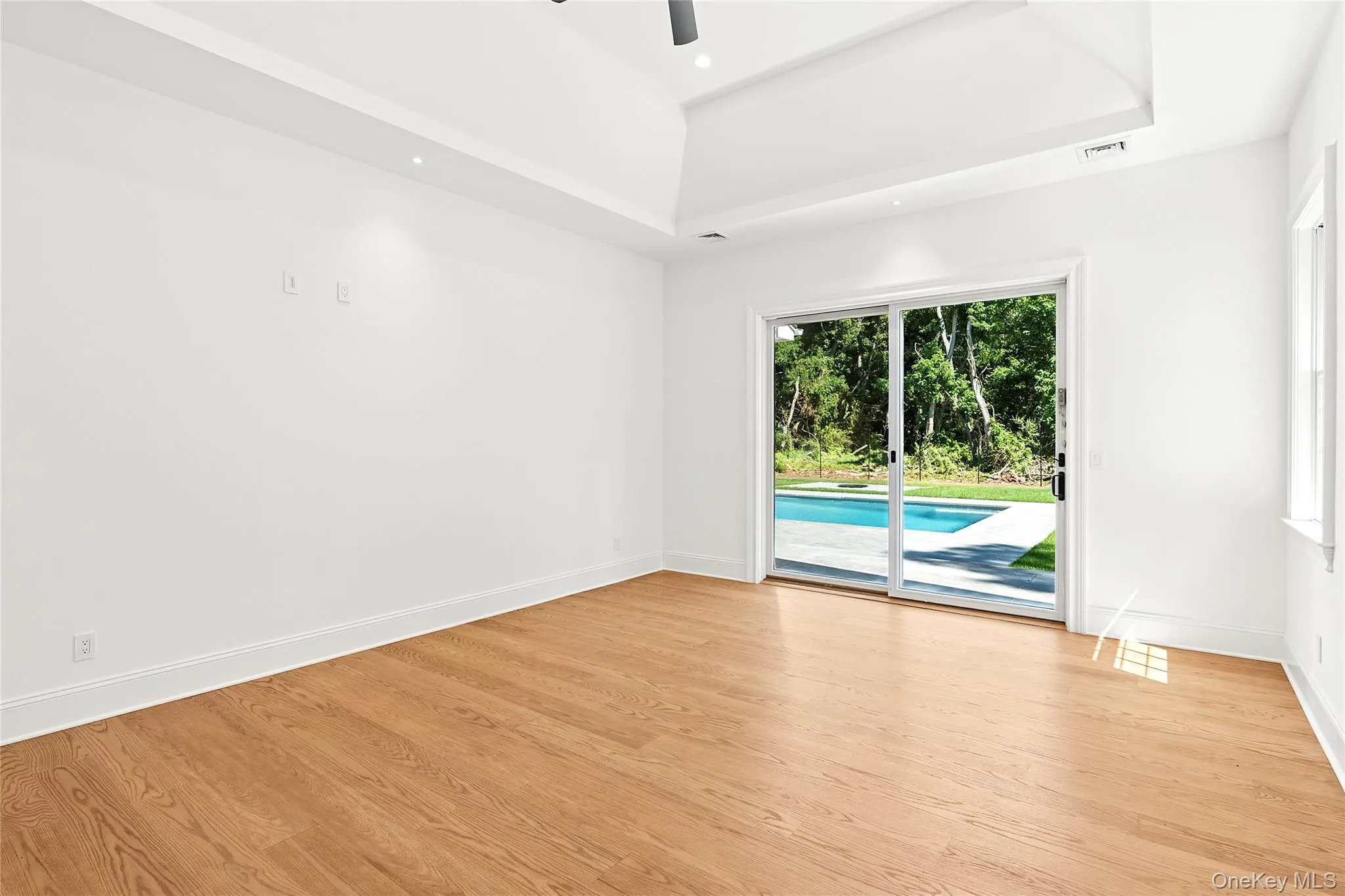 Unfurnished room with ceiling fan, light wood finished floors, a raised ceiling, and recessed lighting Unfurnished room with ceiling fan, light wood finished floors, a raised ceiling, and recessed lighting
