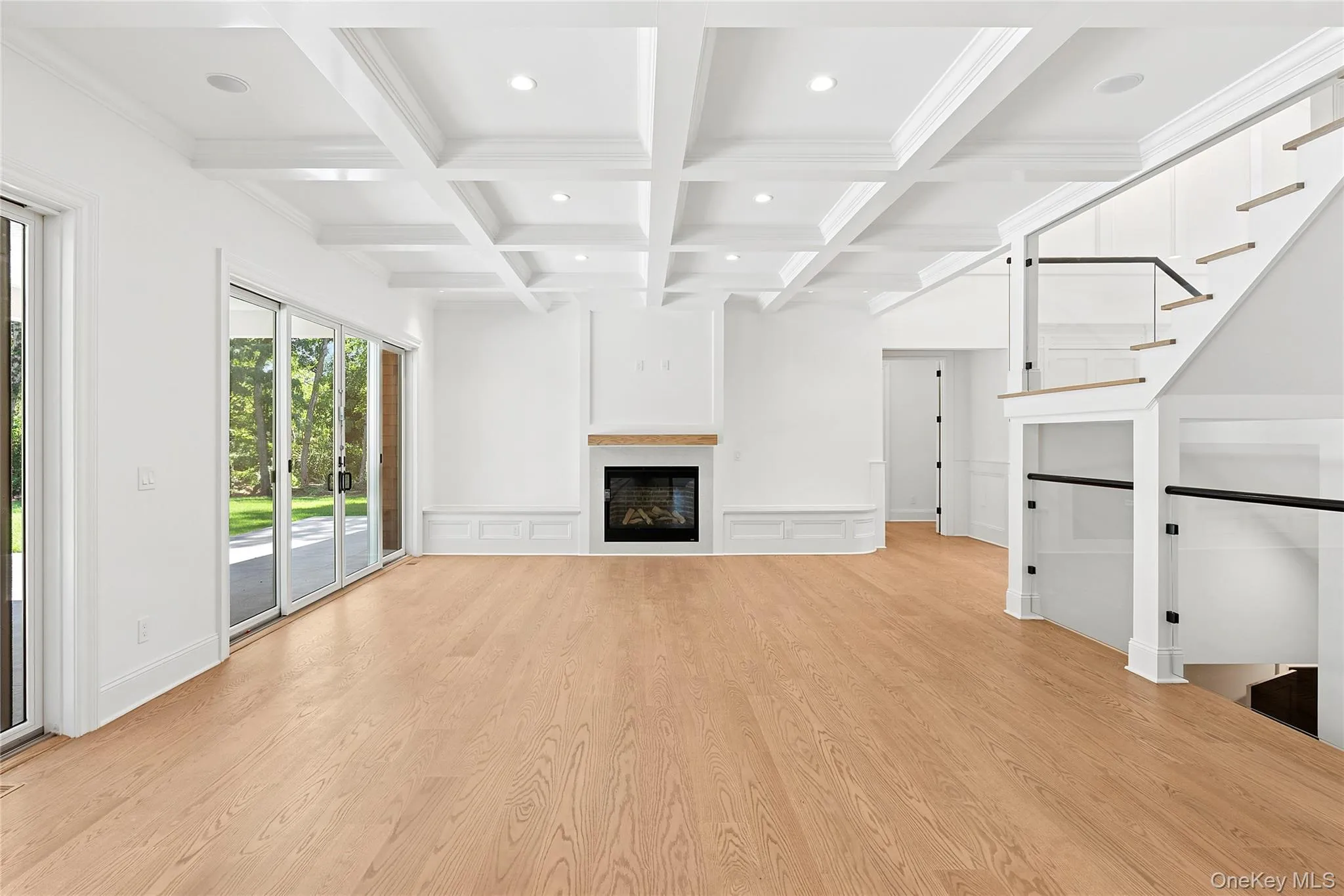 Unfurnished living room with beamed ceiling, coffered ceiling, light wood-style flooring, a fireplace, and a decorative wall Unfurnished living room with beamed ceiling, coffered ceiling, light wood-style flooring, a fireplace, and a decorative wall