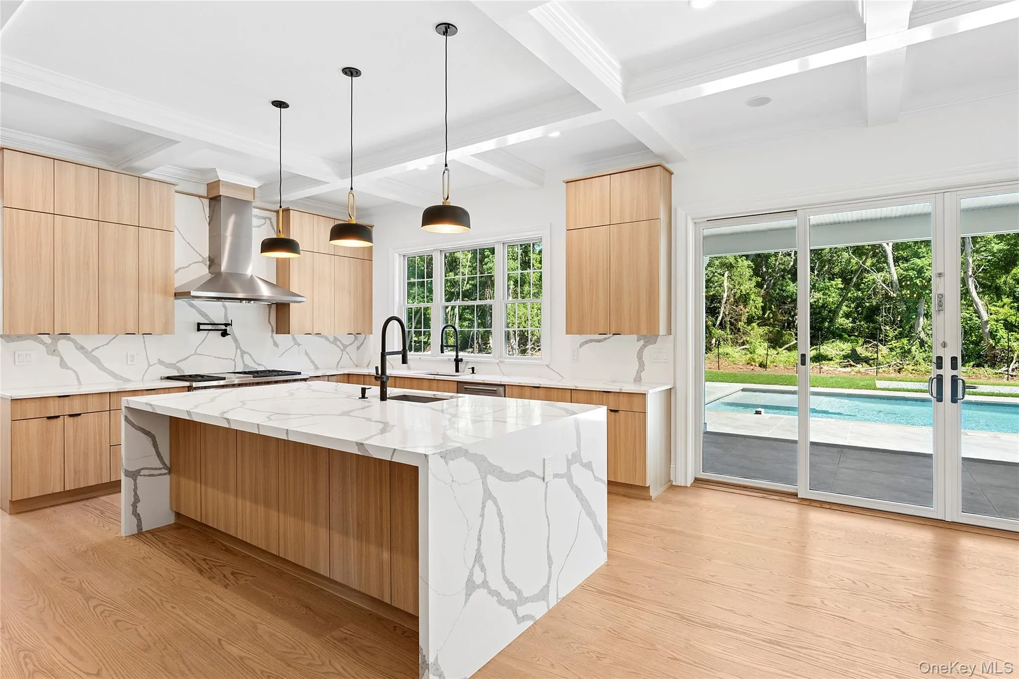 Kitchen featuring modern cabinets, light stone countertops, light wood-style floors, hanging light fixtures, and beamed ceiling Kitchen featuring modern cabinets, light stone countertops, light wood-style floors, hanging light fixtures, and beamed ceiling