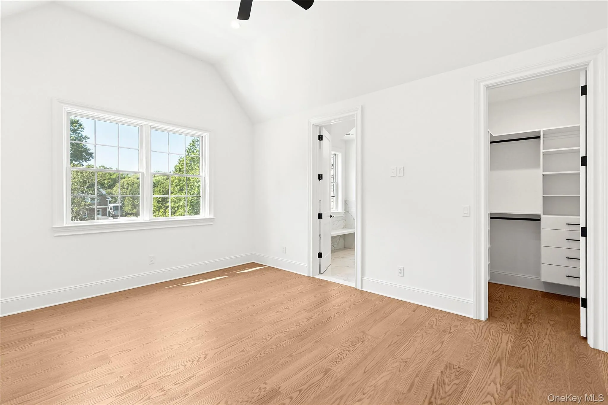 Unfurnished bedroom with vaulted ceiling, light wood finished floors, a spacious closet, a ceiling fan, and ensuite bathroom Unfurnished bedroom with vaulted ceiling, light wood finished floors, a spacious closet, a ceiling fan, and ensuite bathroom