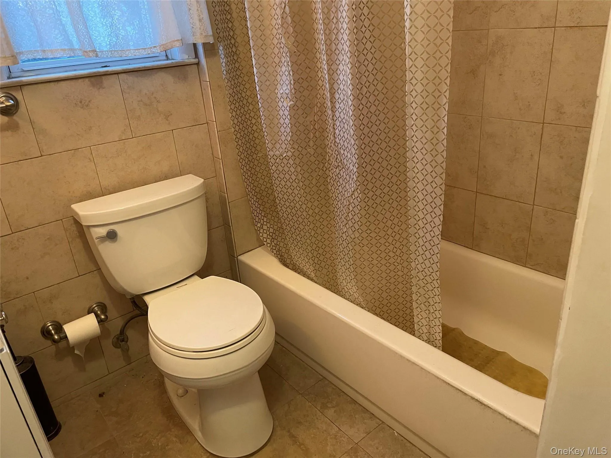 Full bathroom with shower / tub combo, tile walls, and tile patterned floors Full bathroom with shower / tub combo, tile walls, and tile patterned floors