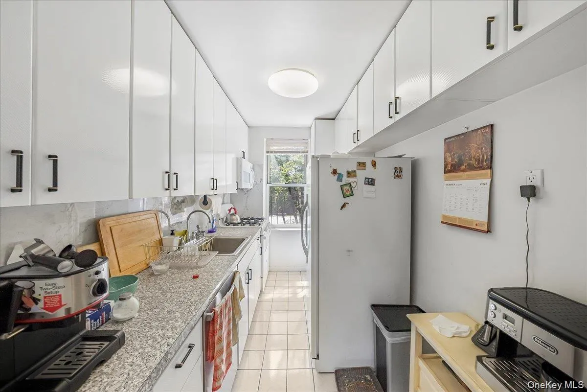 Kitchen featuring white appliances, white cabinets, light tile patterned floors, backsplash, and light stone countertops Kitchen featuring white appliances, white cabinets, light tile patterned floors, backsplash, and light stone countertops