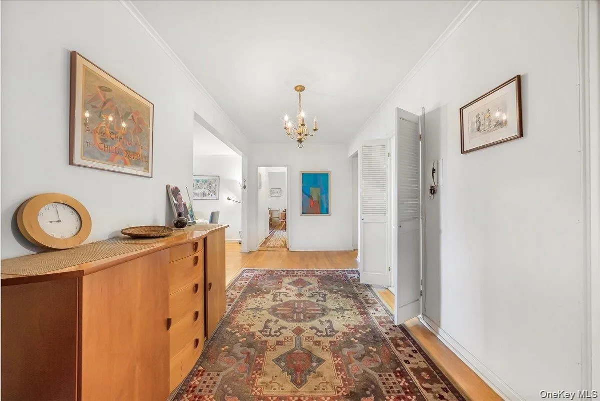 Corridor with crown molding, a chandelier, and light wood-type flooring Corridor with crown molding, a chandelier, and light wood-type flooring