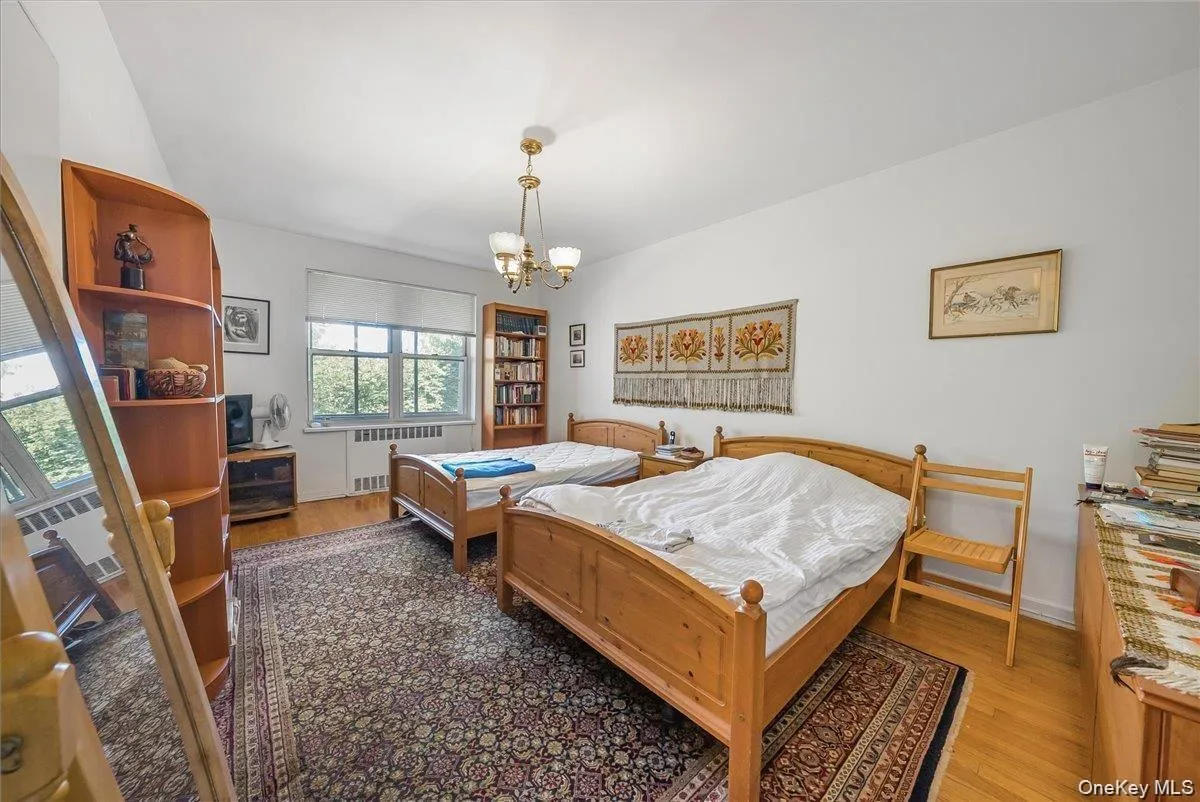 Bedroom featuring wood finished floors, radiator heating unit, and a chandelier Bedroom featuring wood finished floors, radiator heating unit, and a chandelier