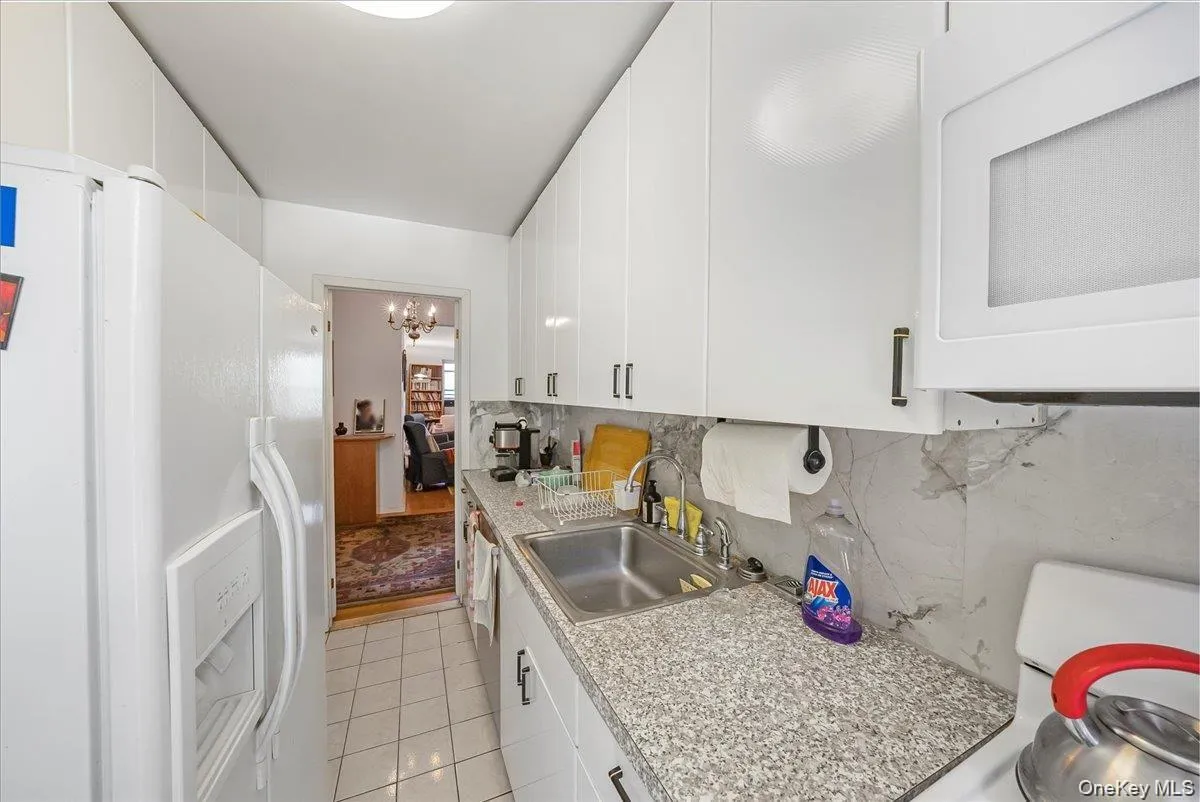 Kitchen with white appliances, backsplash, light countertops, and white cabinetry Kitchen with white appliances, backsplash, light countertops, and white cabinetry
