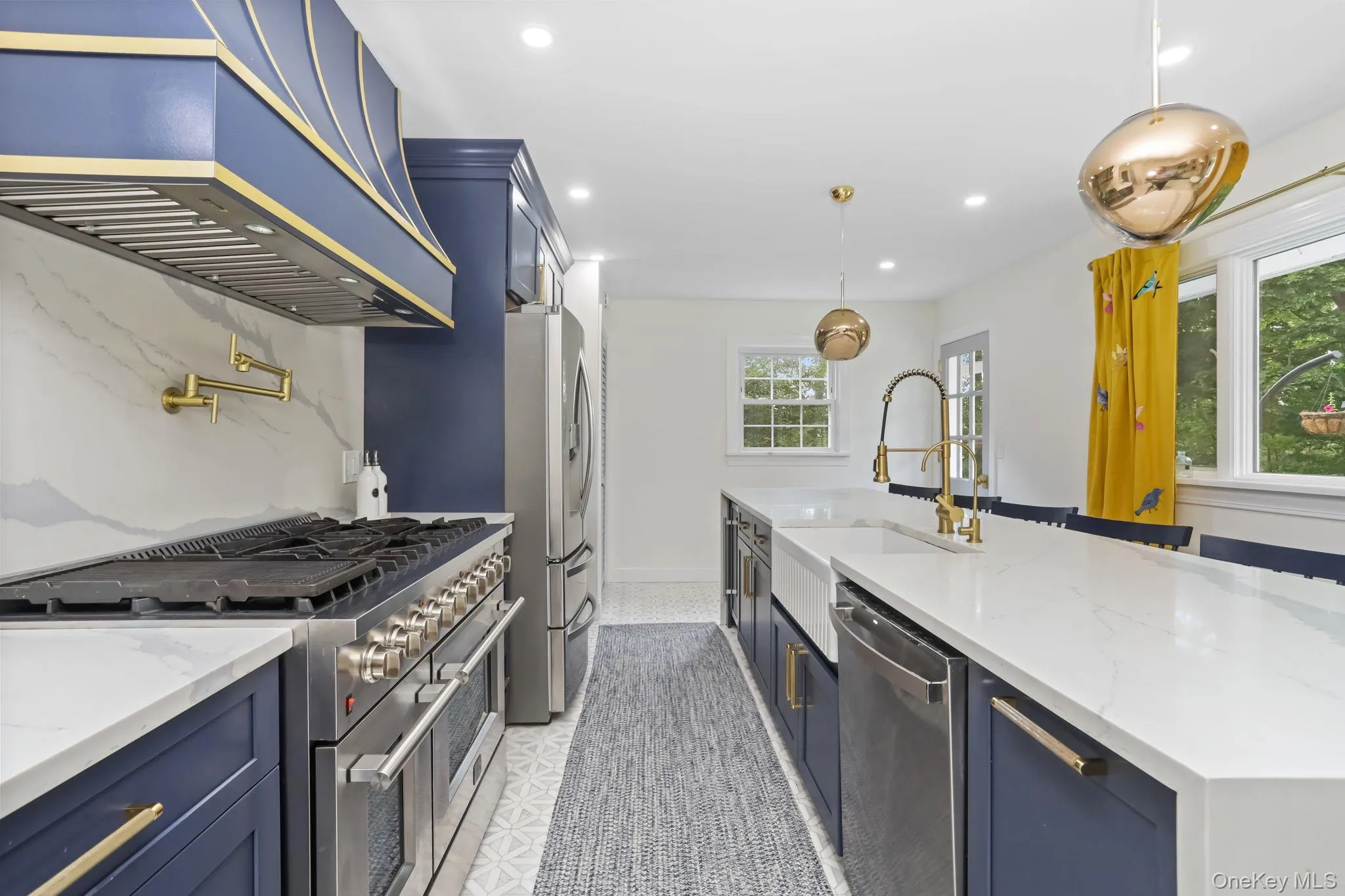 Kitchen with blue cabinets, appliances with stainless steel finishes, light stone countertops, custom exhaust hood, and recessed lighting Kitchen with blue cabinets, appliances with stainless steel finishes, light stone countertops, custom exhaust hood, and recessed lighting