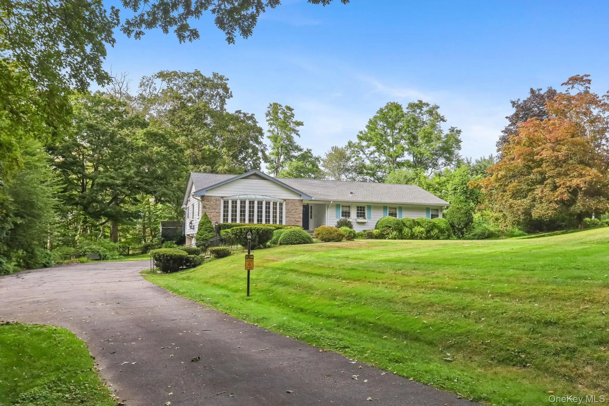 Ranch-style home with a front lawn, driveway, and view of wooded area Ranch-style home with a front lawn, driveway, and view of wooded area