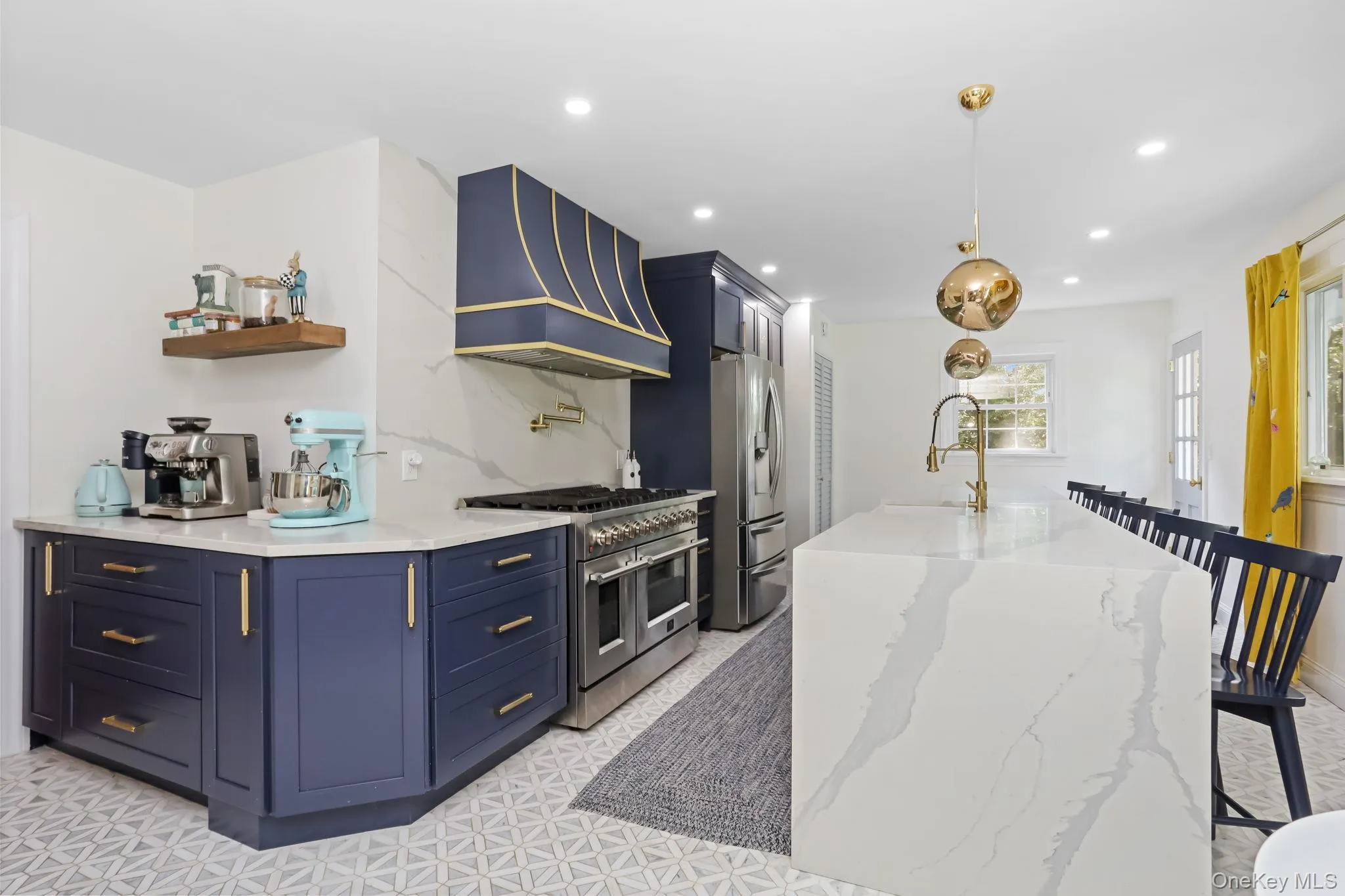 Kitchen featuring light stone countertops, appliances with stainless steel finishes, custom exhaust hood, a center island with sink, and decorative light fixtures Kitchen featuring light stone countertops, appliances with stainless steel finishes, custom exhaust hood, a center island with sink, and decorative light fixtures