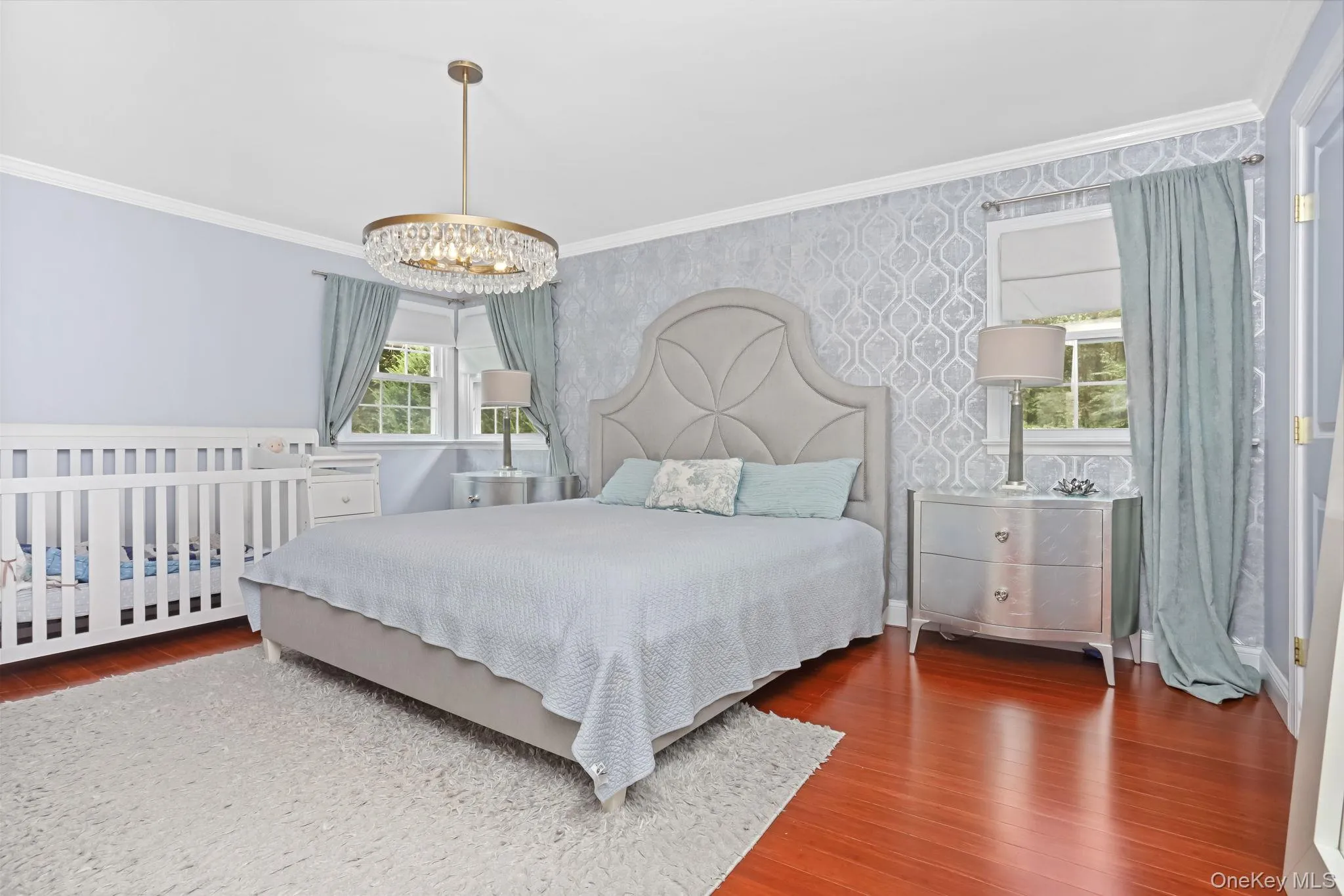 Primary bedroom featuring ornamental molding, multiple windows, wood finished floors, wallpapered walls, and a chandelier Primary bedroom featuring ornamental molding, multiple windows, wood finished floors, wallpapered walls, and a chandelier