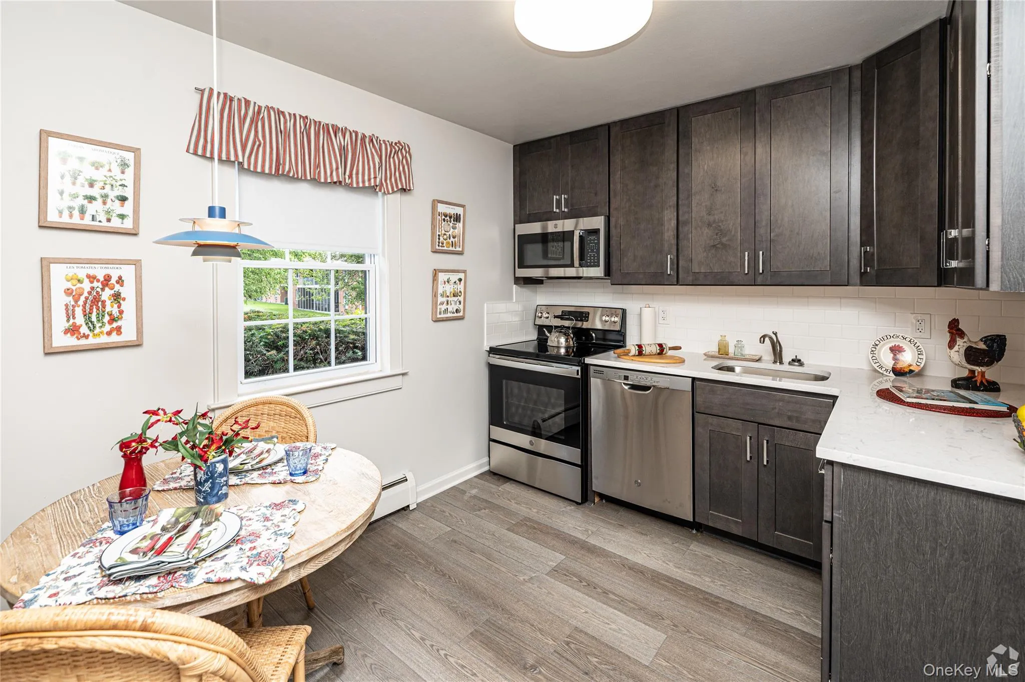 Kitchen with dark brown cabinetry, appliances with stainless steel finishes, pendant lighting, light wood-style floors, and light stone counters Kitchen with dark brown cabinetry, appliances with stainless steel finishes, pendant lighting, light wood-style floors, and light stone counters